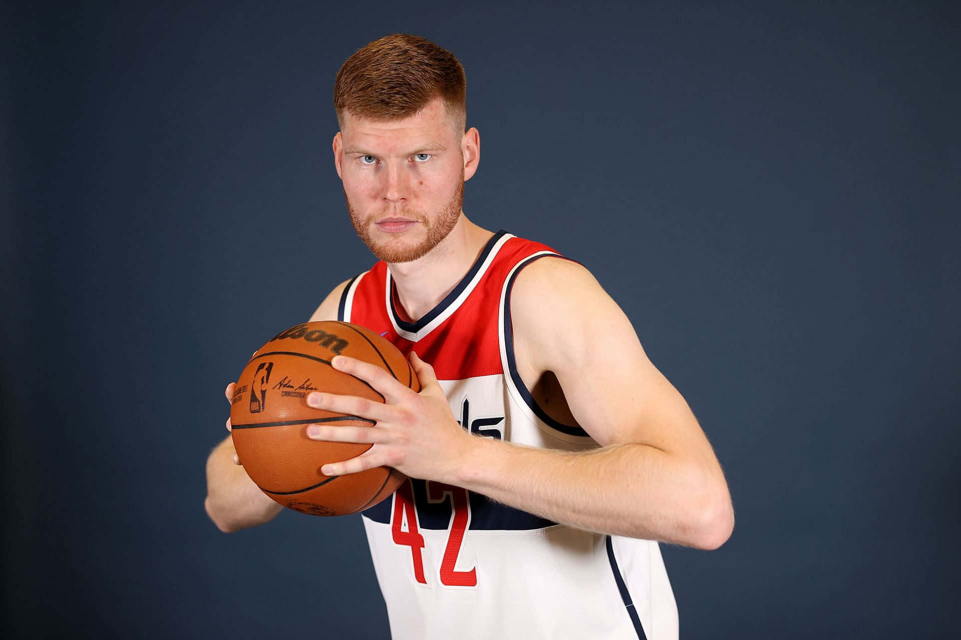 NBA 桌布 壁紙 — 一位肌肉發達的籃球運動員身穿紅白球衣，在深藍色攝影棚背景下手持籃球。