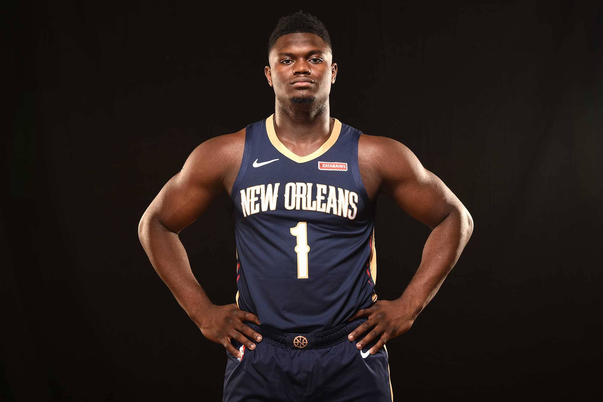 Zion 桌布 壁紙 — 一位肌肉發達的籃球運動員身穿紐奧良球衣，雙手叉腰，自信地站在黑色背景前。