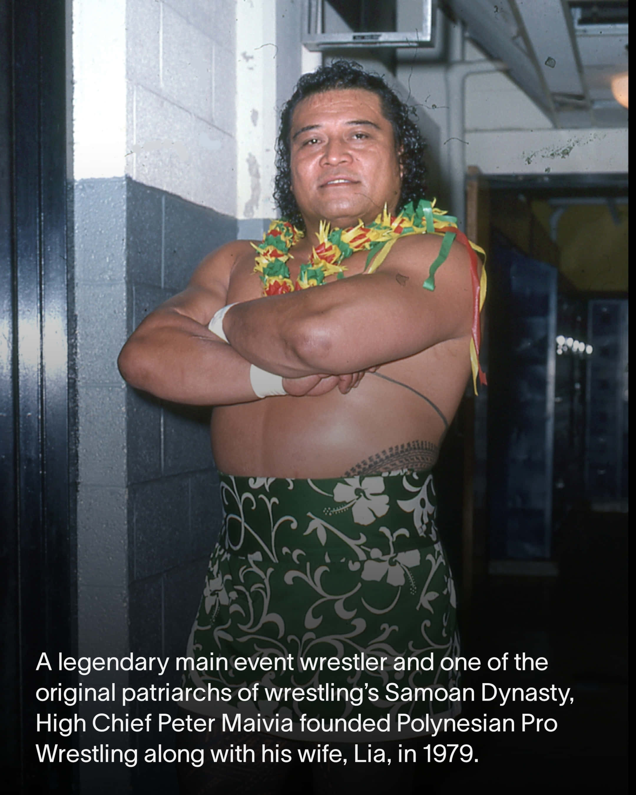 Peter Maivia 桌布 壁紙 — 一位肌肉發達的薩摩亞摔角手穿著花卉裙和花環，自信地交叉雙臂站在後台走廊。