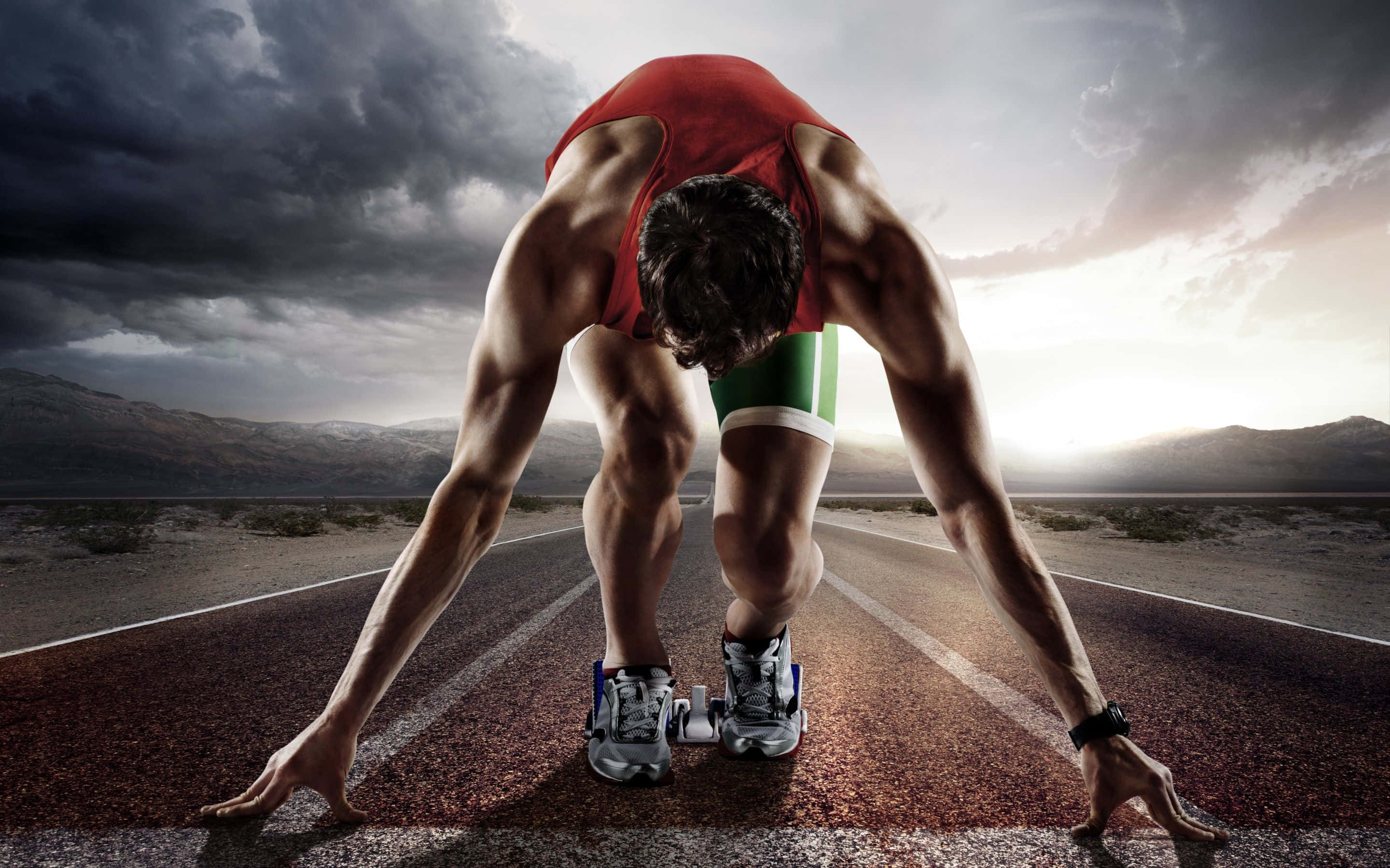 Athlete 桌布 壁紙 — 一位肌肉發達的跑者身穿紅色和綠色裝備，在戲劇性的暴風雨天空下蹲在沙漠道路的起跑線上。