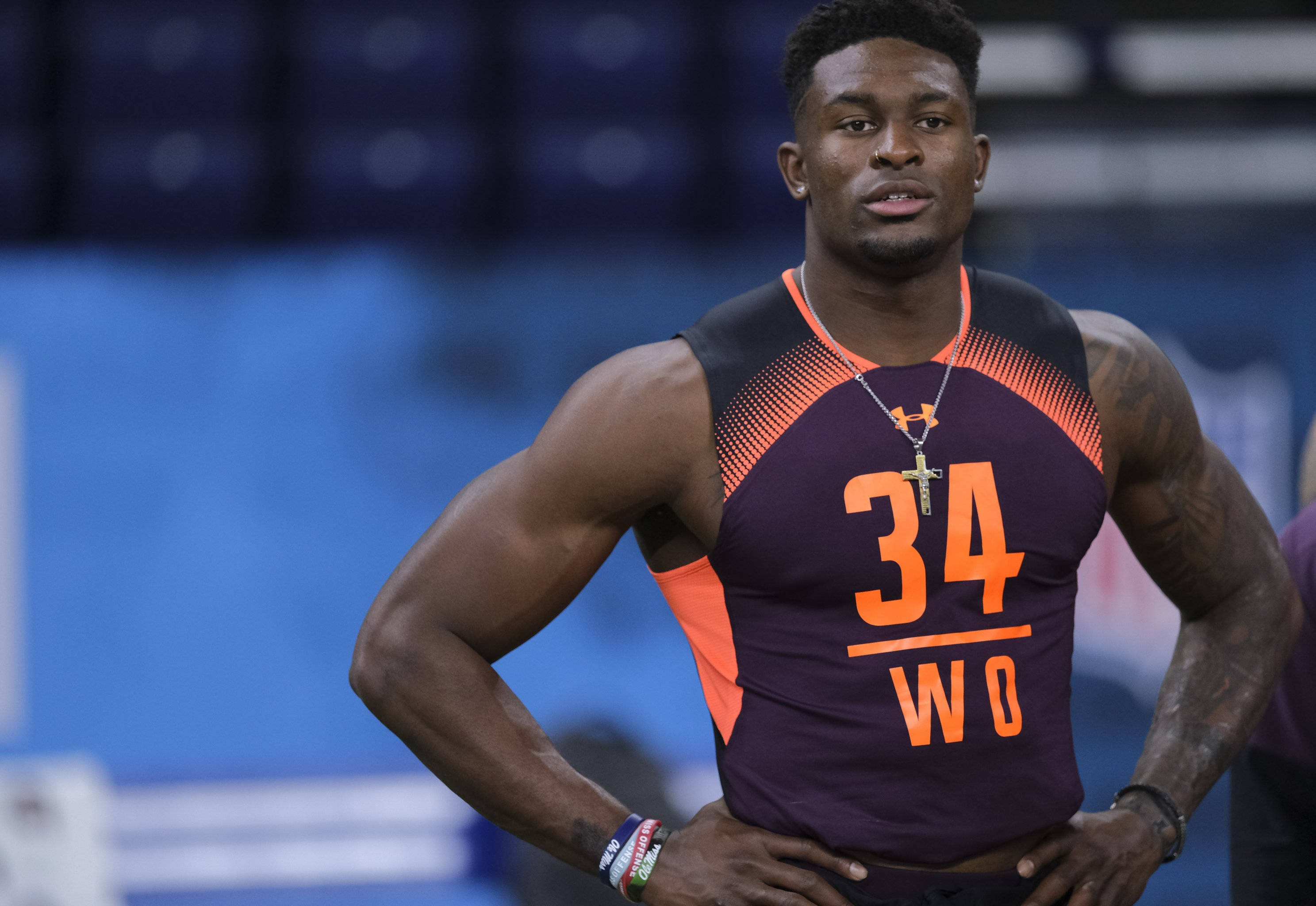 Dk 桌布 壁紙 — 一位肌肉發達的運動員穿著紫色和橙色相間的34號球衣，雙手叉腰自信地站在室內場館。