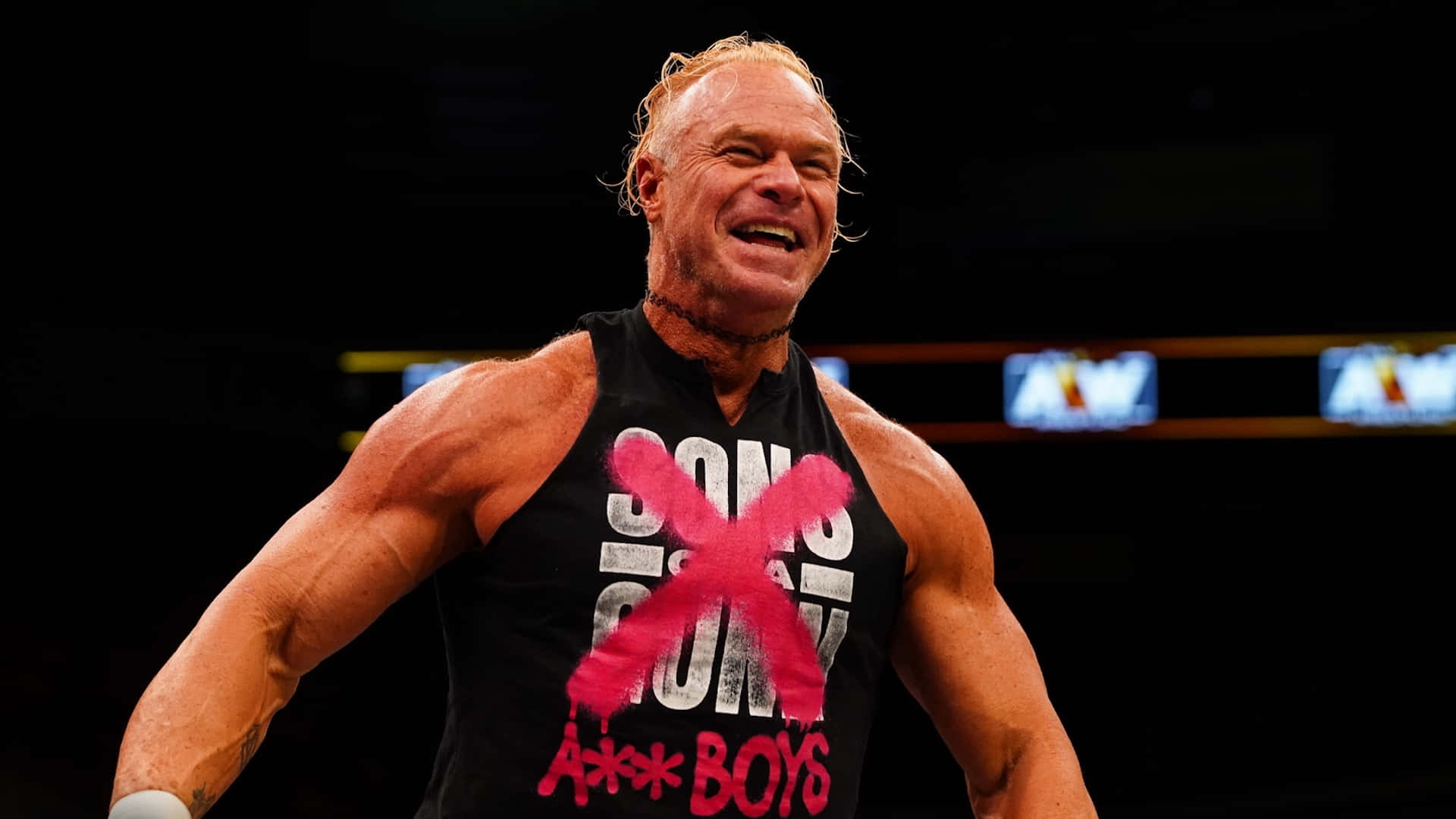 WWE 桌布 壁紙 — 一位肌肉發達的金髮摔角手在黑暗的擂台上穿著帶有紅色塗鴉的黑色背心，勝利地大笑。