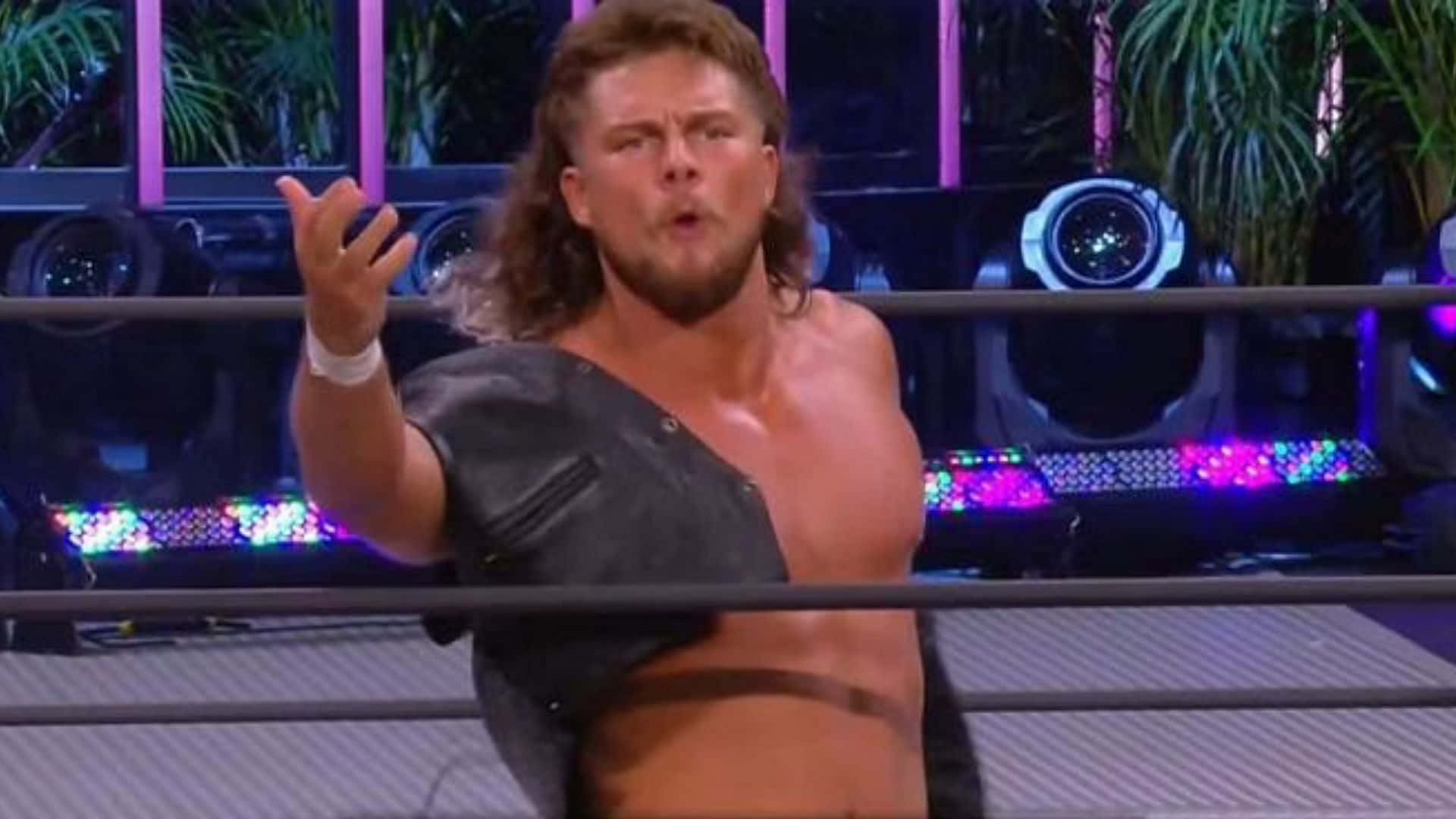 WWE 桌布 壁紙 — 一位肌肉發達的長髮摔角手在色彩繽紛的舞台燈光下，在擂台上戲劇性地做手勢。
