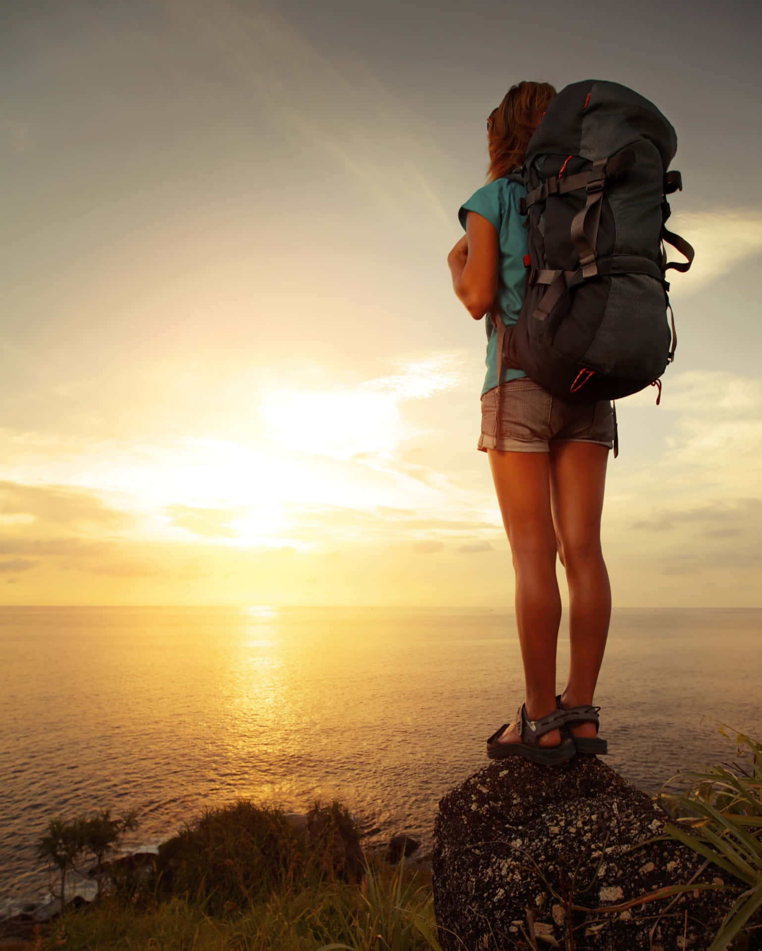Traveling 桌布 壁紙 — 一位背著大背包的旅客站在岩石峭壁上，俯瞰著日落時金色的海洋。