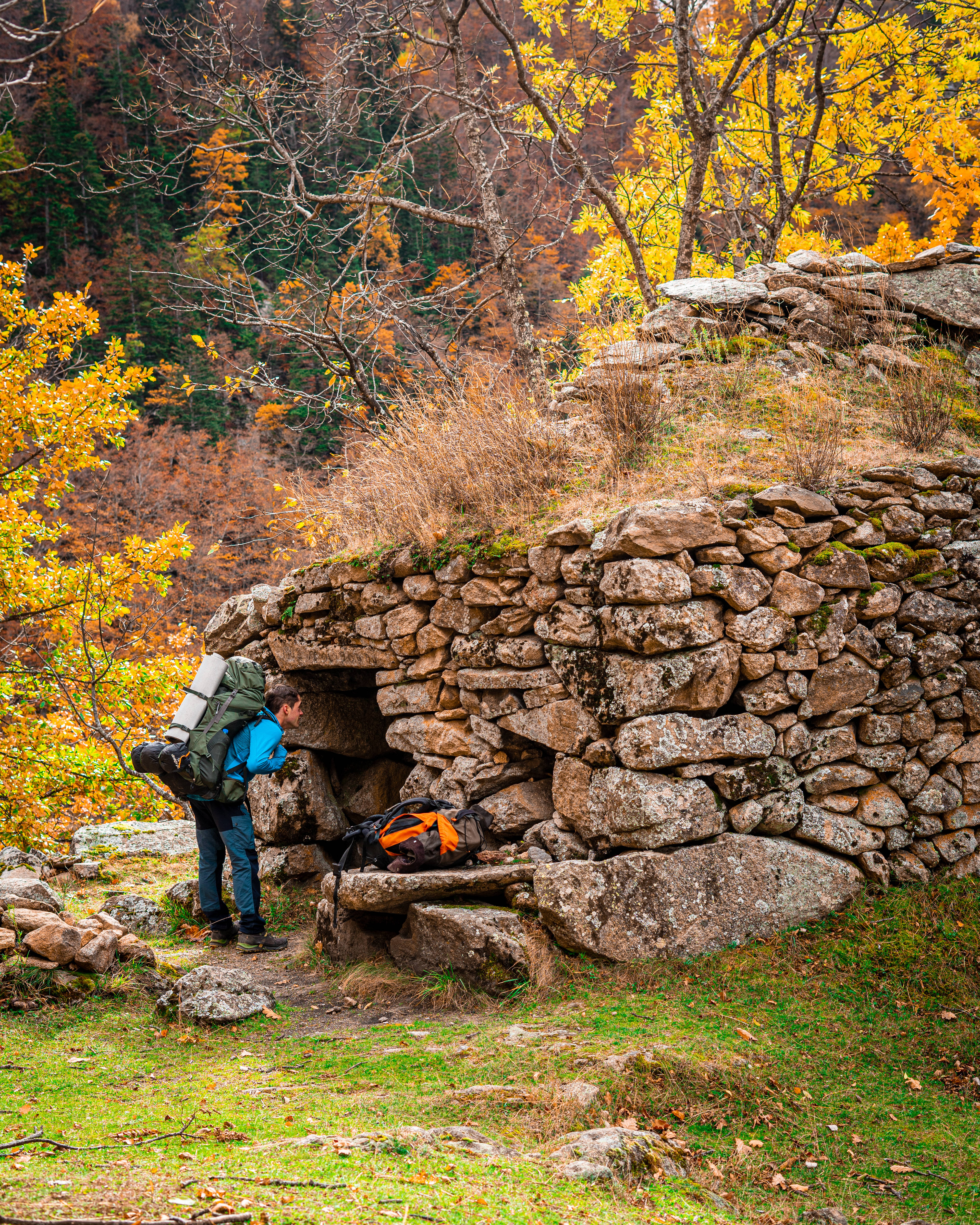Best Autumn 桌布 壁紙 — 一位背著大背包的遠足者正在探索一座坐落在充滿活力的秋日森林中的古老石頭廢墟。