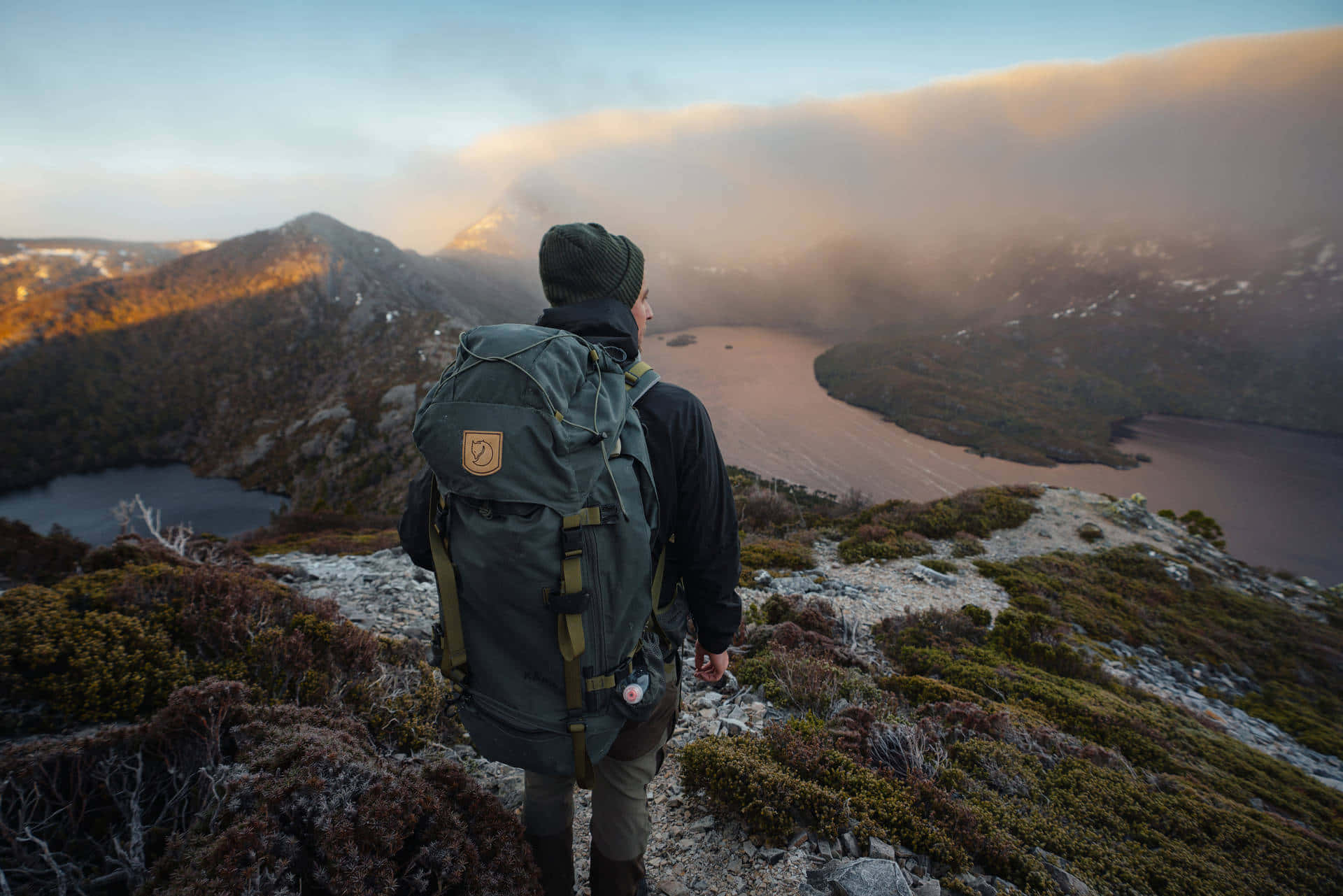 Hiking 桌布 壁紙 — 一位背著大背包的遠足者站在崎嶇的山脊上，俯瞰黃金時段霧氣繚繞的山谷和湖泊。