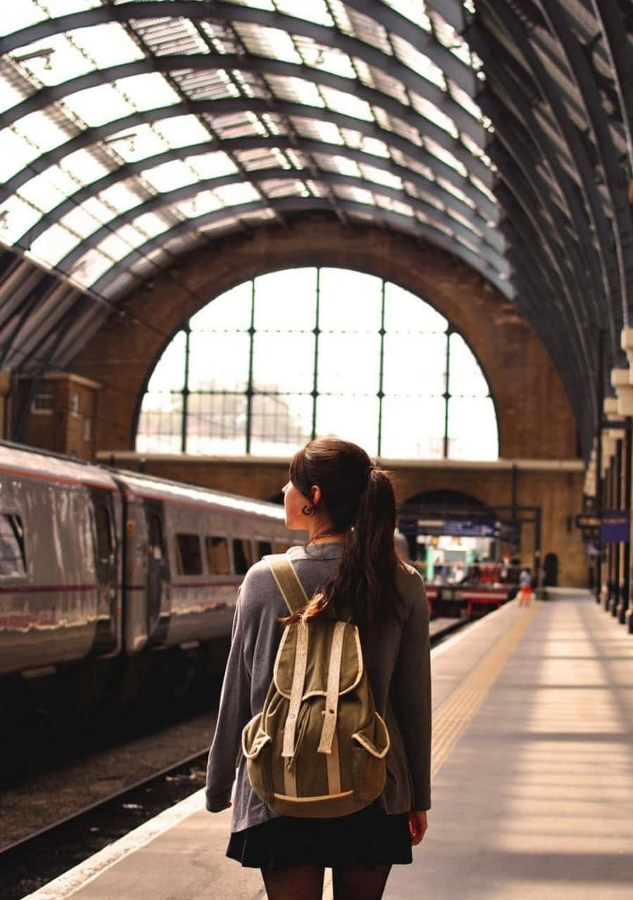 Train Station 桌布 壁紙 — 一位背著背包的年輕女士站在宏偉拱形玻璃屋頂下的陽光火車月台上。
