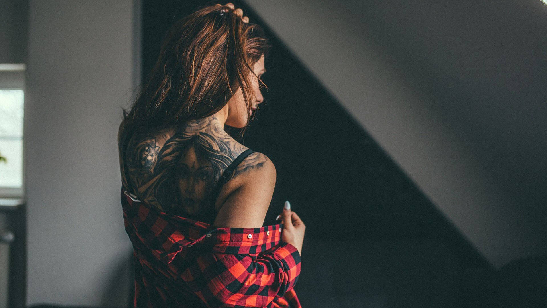 Tattoo 桌布 壁紙 — 一位背部有複雜刺青的女性站在昏暗的房間裡，掀起紅色格子襯衫以展示她的藝術作品。