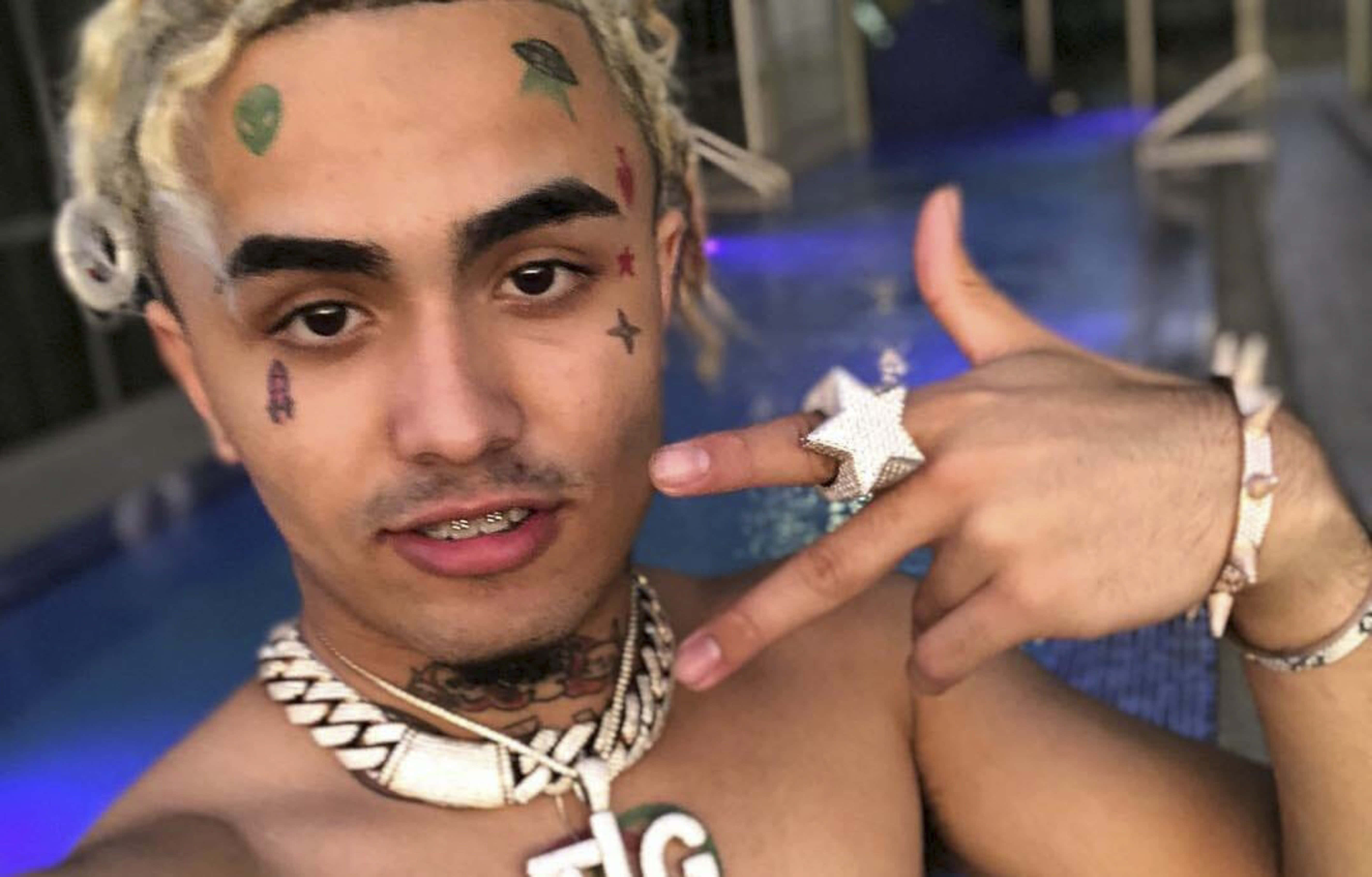 桌布 壁紙 — 一位臉上刺青、戴著星星戒指的年輕男子，夜晚在泳池邊自信地擺姿勢。