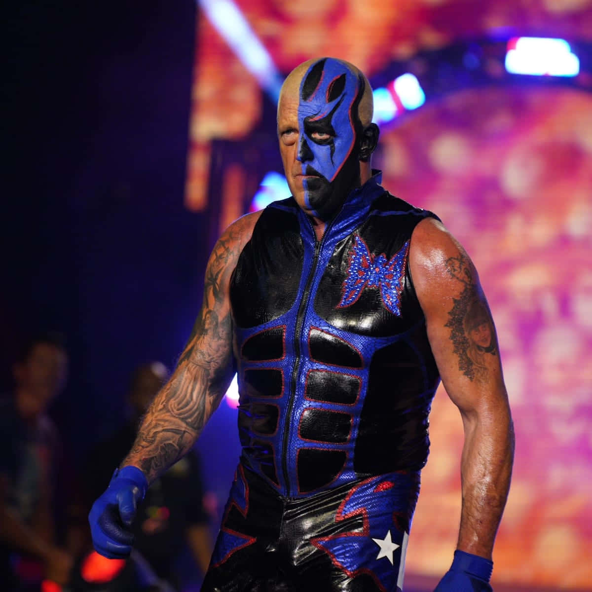 WWE 桌布 壁紙 — 一位臉上塗有藍黑顏料、身穿愛國服裝的摔角手自信地站在舞台燈光下。