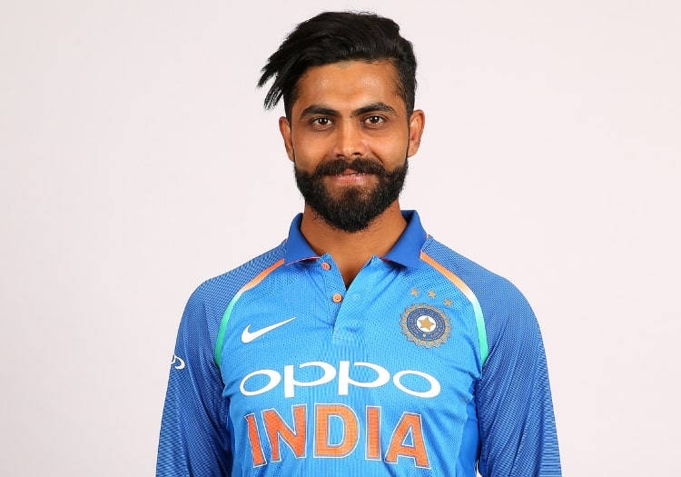  壁紙 — 一位自信的印度板球運動員穿著藍色隊服，上面有'INDIA'和贊助商標誌，在純白色背景前擺姿勢。