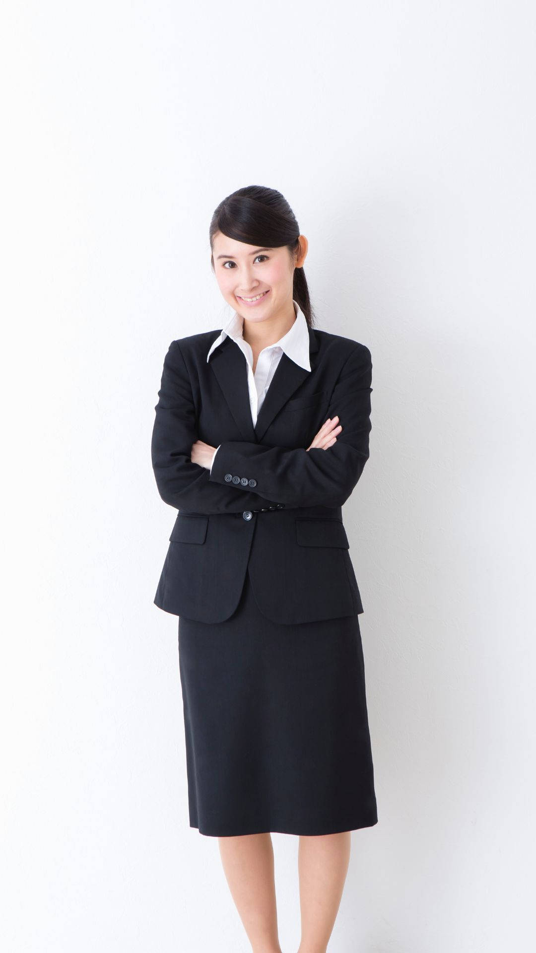 黑色 桌布 壁紙 — 一位自信的商務女性穿著黑色西裝，在純白背景前交叉雙臂微笑。