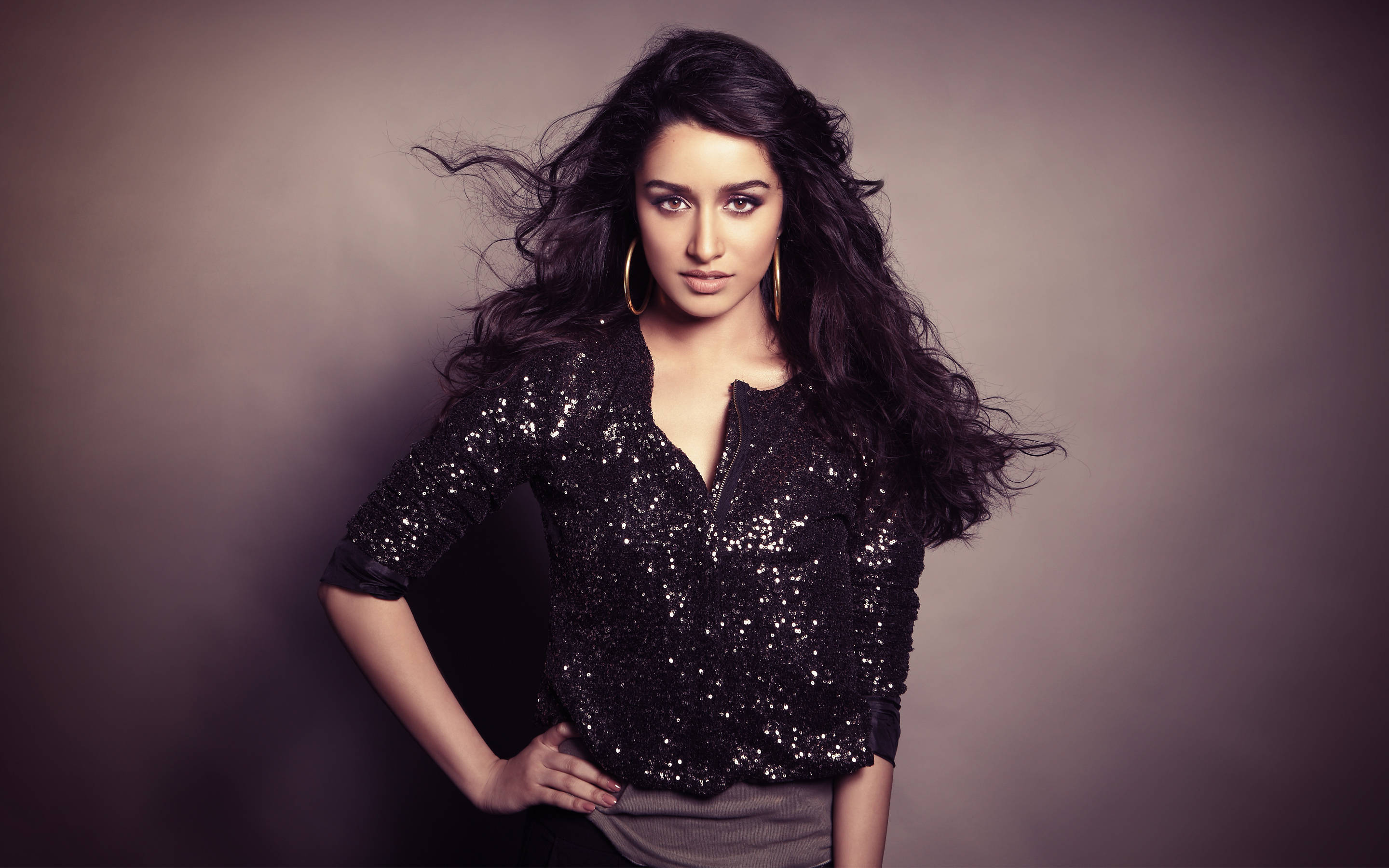 Shraddha Kapoor 桌布 壁紙 — 一位自信的女士擁有一頭飄逸的深色頭髮，在柔和的灰色工作室背景下穿著閃亮的黑色上衣。