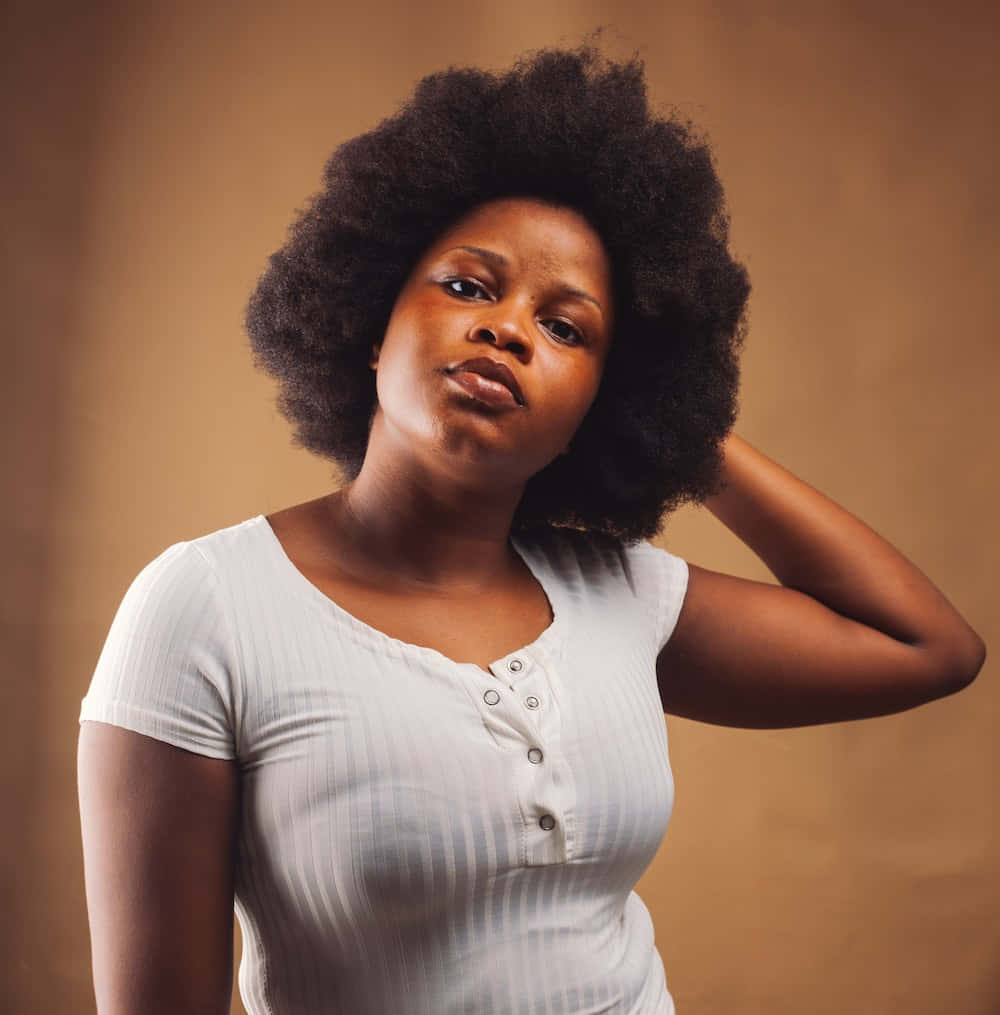Nigeria 桌布 壁紙 — 一位自信的女性，擁有濃密的非洲式頭髮，在溫暖的棕色工作室背景前，穿著白色羅紋上衣擺姿勢。
