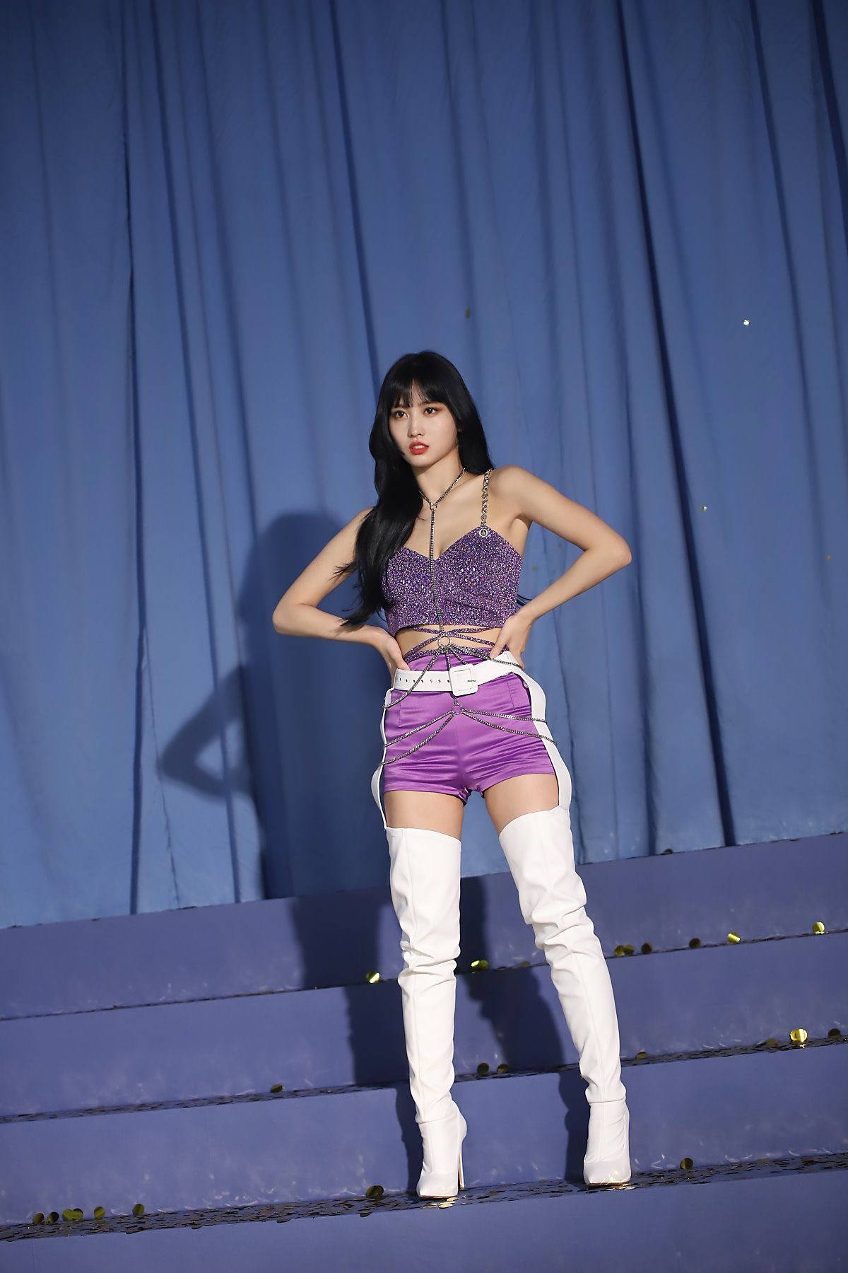 Momo 桌布 壁紙 — 一位自信的女性穿著紫色閃亮上衣和白色過膝靴，在藍色階梯上擺姿勢，背景是垂簾帷幕。