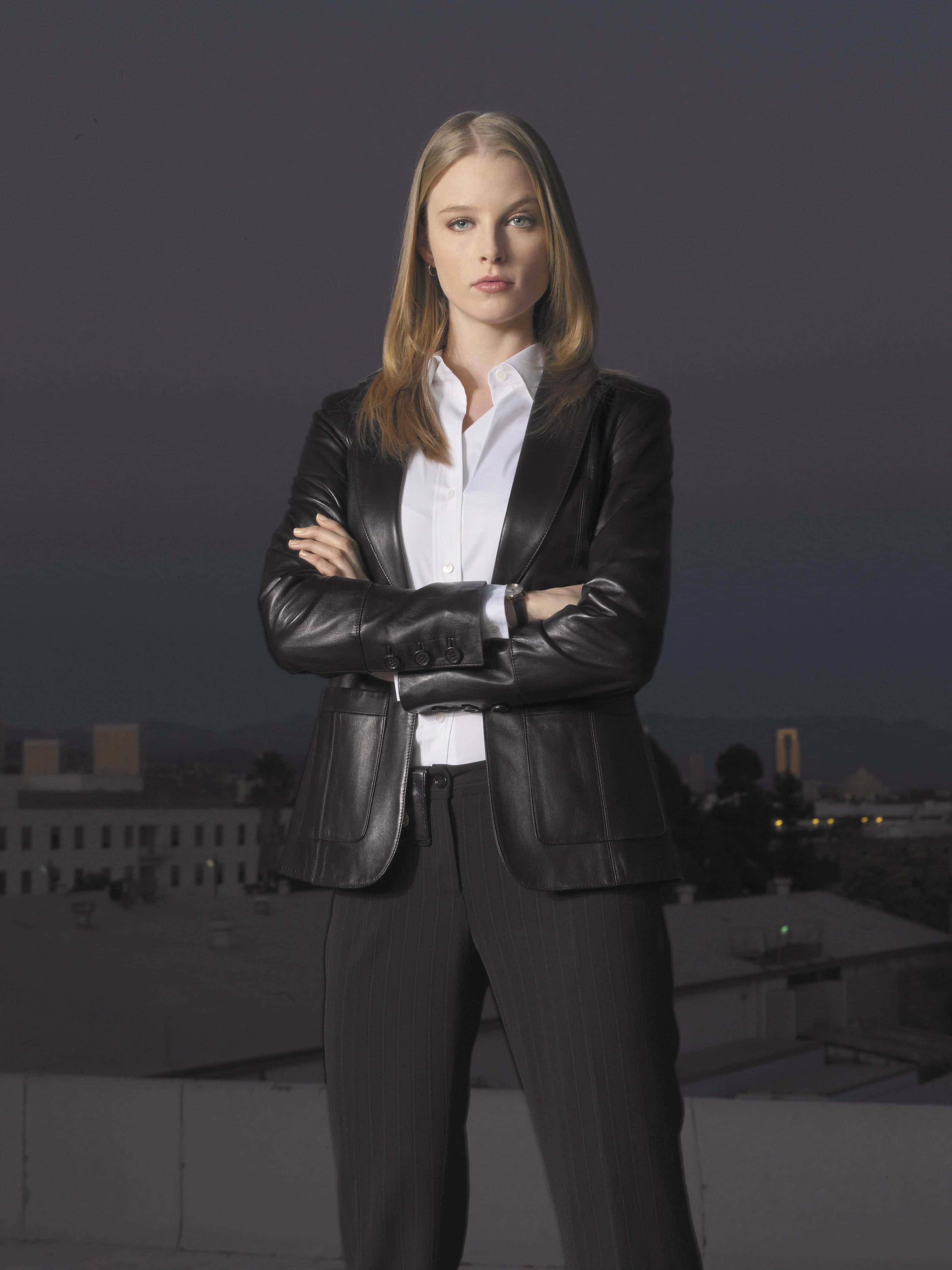 rachel nichols 桌布 壁紙 — 一位自信的女性穿著黑色皮革西裝外套，在黃昏時分雙臂交叉站在城市屋頂上。