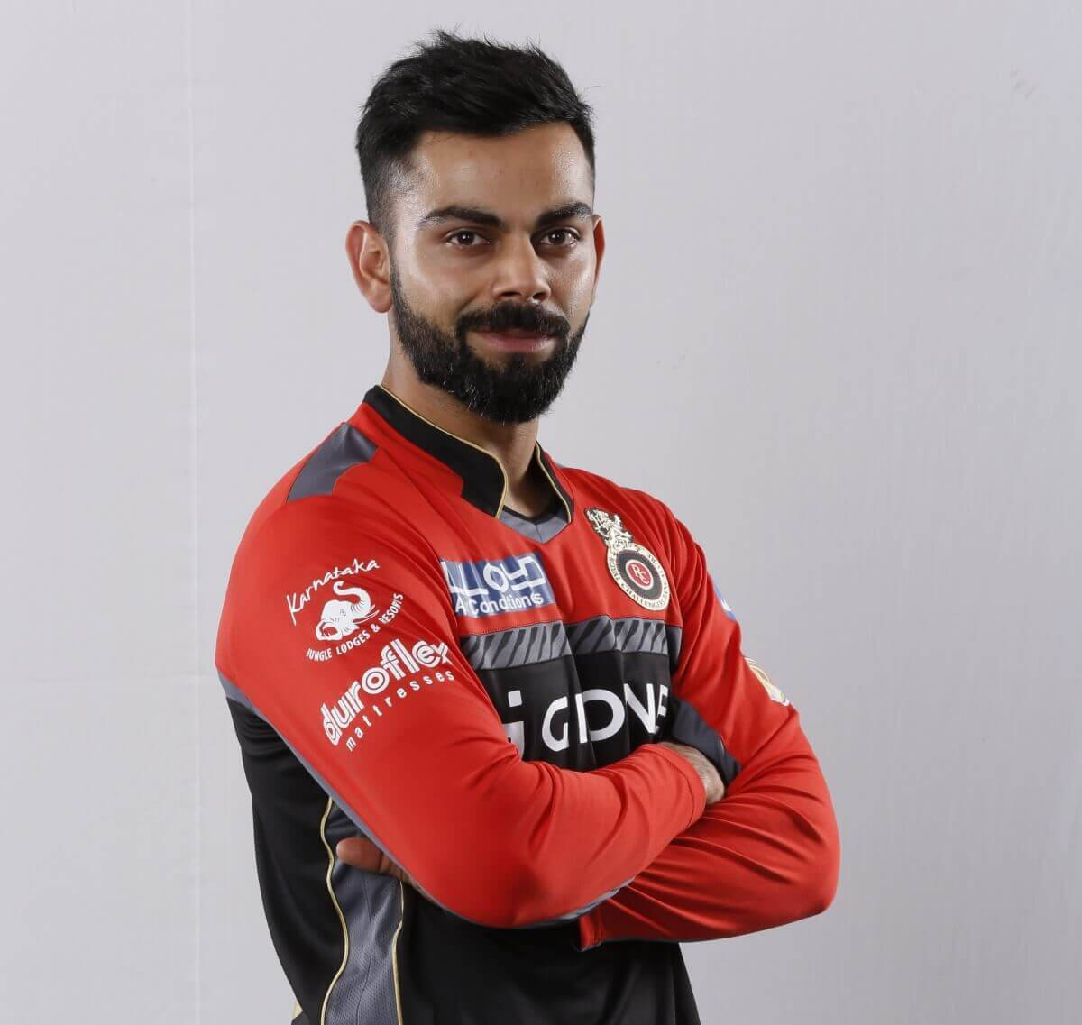 royal challengers bangalore 桌布 壁紙 — 一位自信的板球球員，身穿紅黑球衣，雙手交叉站在純白背景前。