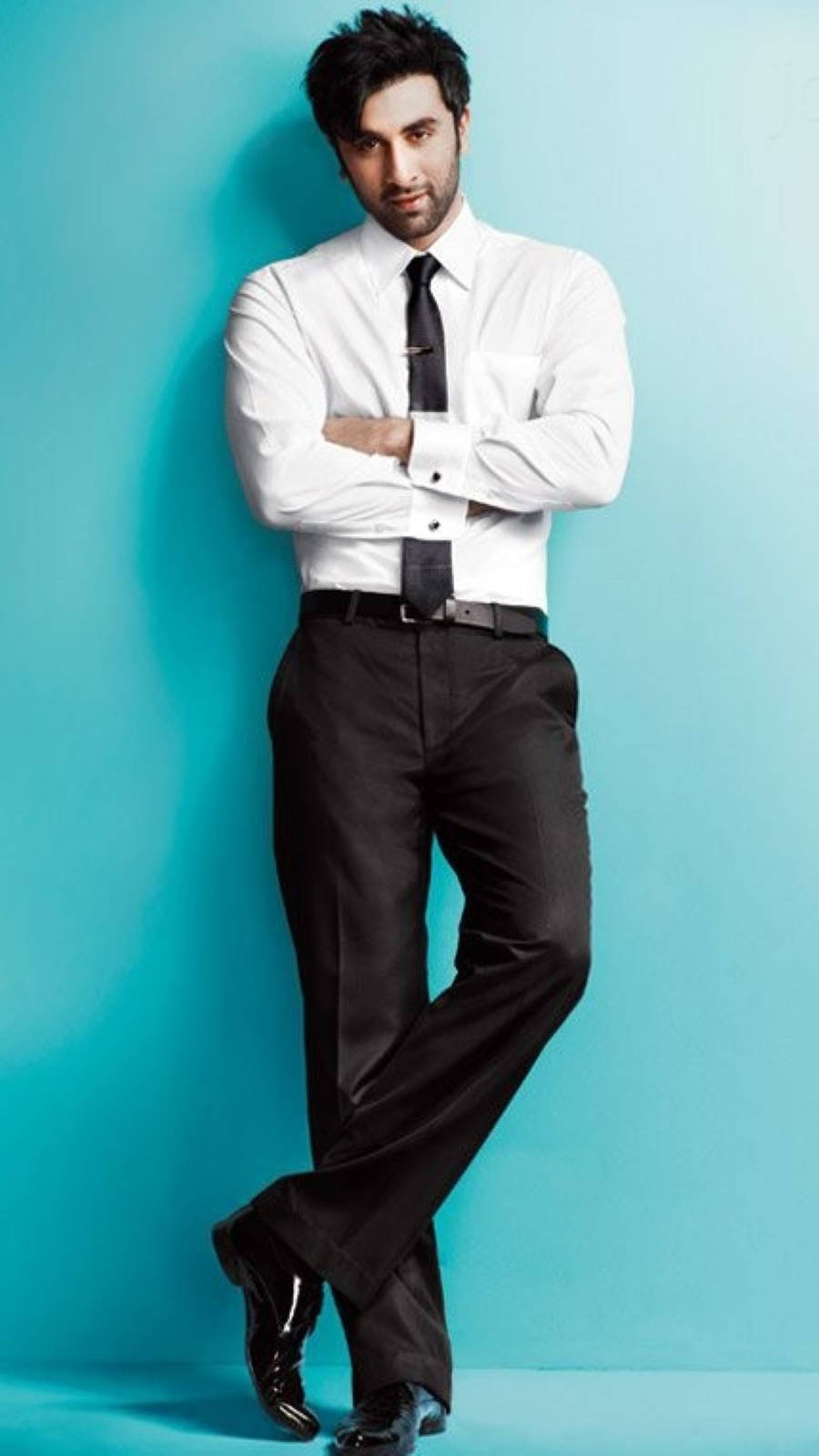 Ranbir Kapoor 桌布 壁紙 — 一位自信的男人，穿著一件清爽的白襯衫和黑色領帶，雙手交叉站在一個充滿活力的藍綠色攝影棚背景前。