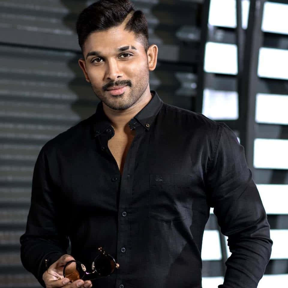 Allu Arjun 桌布 壁紙 — 一位自信的男人穿著黑色襯衫，在現代幾何背景前拿著太陽眼鏡。
