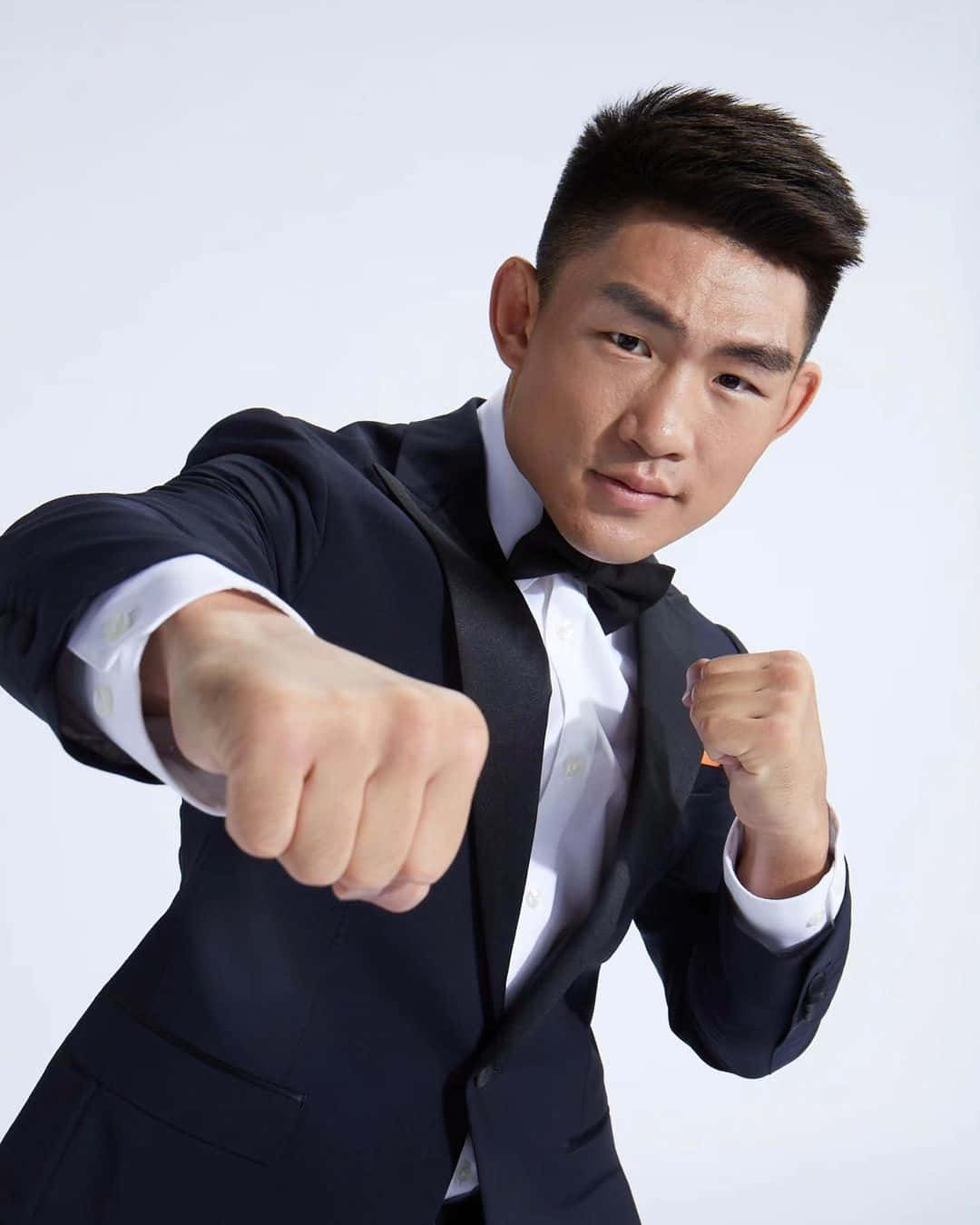 人像動態 桌布 壁紙 — 一位自信的男士穿著剪裁俐落的黑色禮服，在純白背景前擺出強勁的拳擊姿勢。