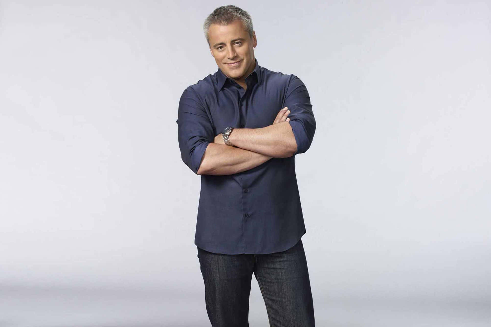 Matt Leblanc 桌布 壁紙 — 一位自信的男士穿著海軍藍色襯衫，站在純淺灰色的攝影棚背景前交叉雙臂。