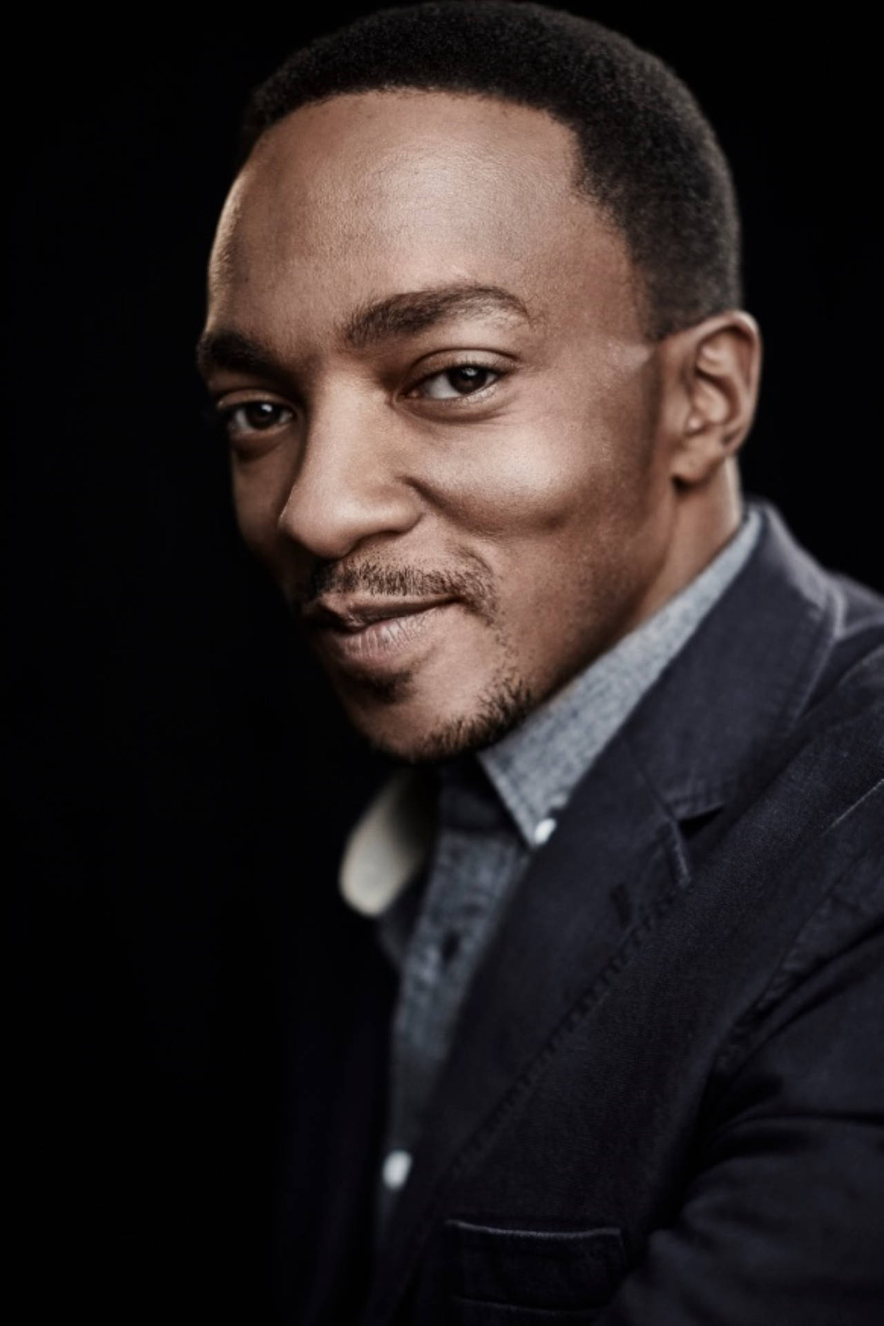 Anthony Mackie 桌布 壁紙 — 一位自信的男士穿著深色西裝，在黑色背景前的攝影棚肖像中溫暖地微笑。