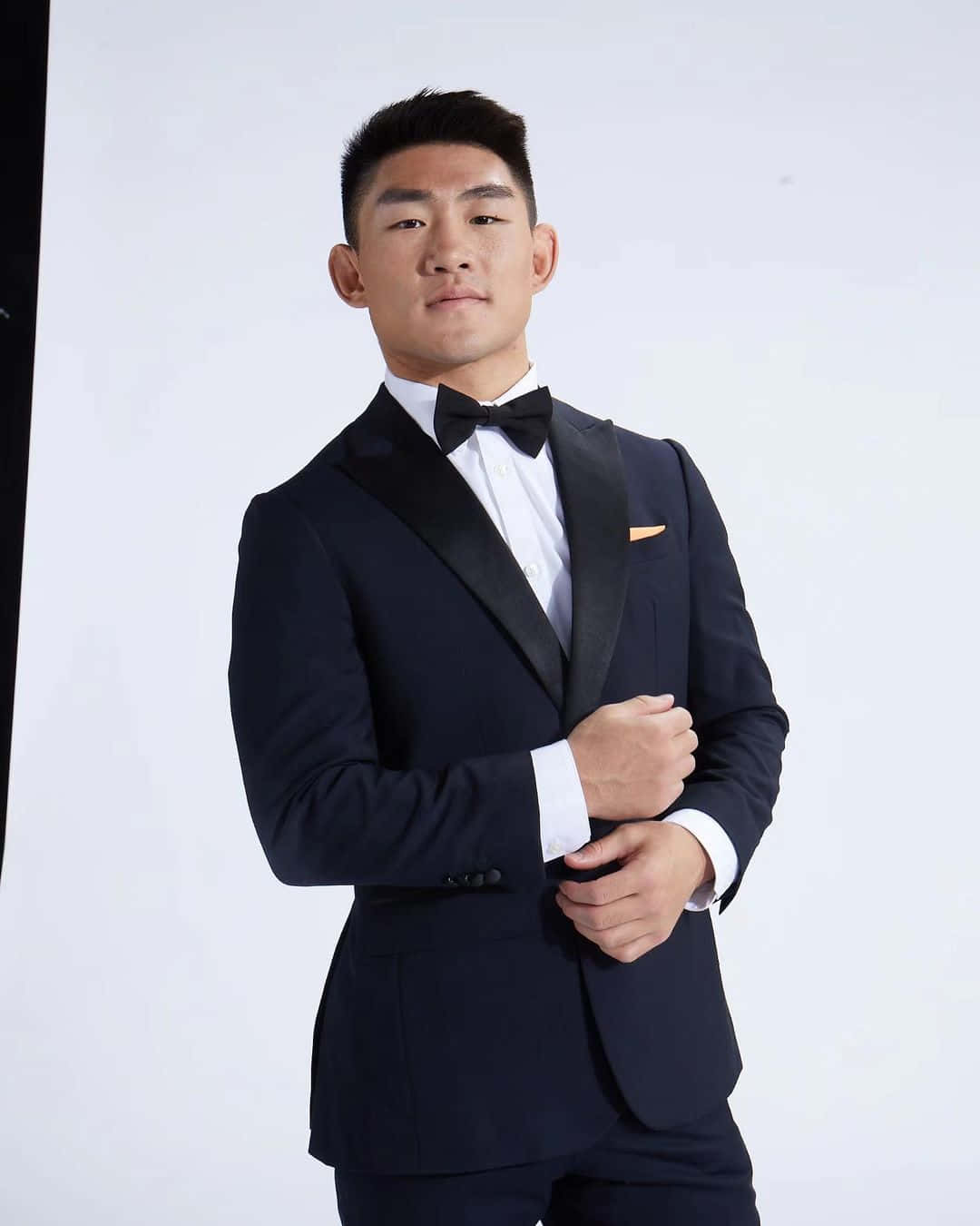 人像動態 桌布 壁紙 — 一位自信的男士穿著黑色禮服和蝴蝶結，站在純白背景前。