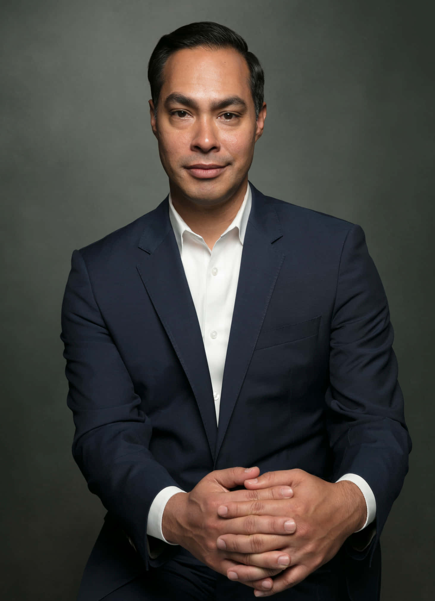 Celebrity 桌布 壁紙 — 一位自信的男士身穿海軍藍西裝和白襯衫，在柔和的灰色攝影棚背景前交疊雙手擺姿勢。