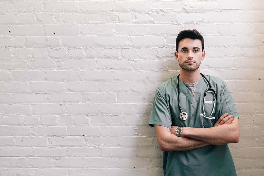 Nurse 桌布 壁紙 — 一位自信的男醫生穿著綠色手術衣，雙手交叉，頸上掛著聽診器，靠著白色磚牆。