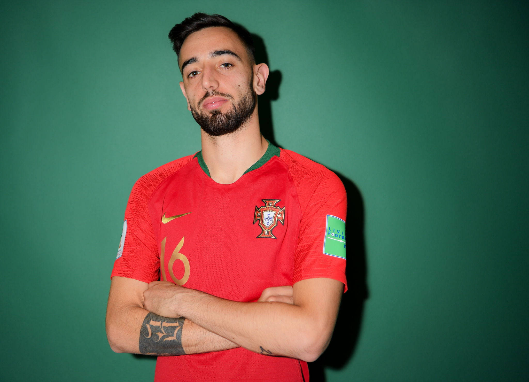 Portugal 桌布 壁紙 — 一位自信的足球員身穿紅色葡萄牙球衣，在純綠色背景前交叉雙臂站立。