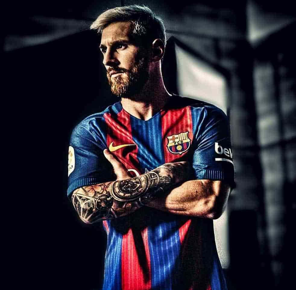 Messi Cool 桌布 壁紙 — 一位自信的足球員身穿紅藍條紋球衣，在黑暗的工業背景下交叉雙臂站立。