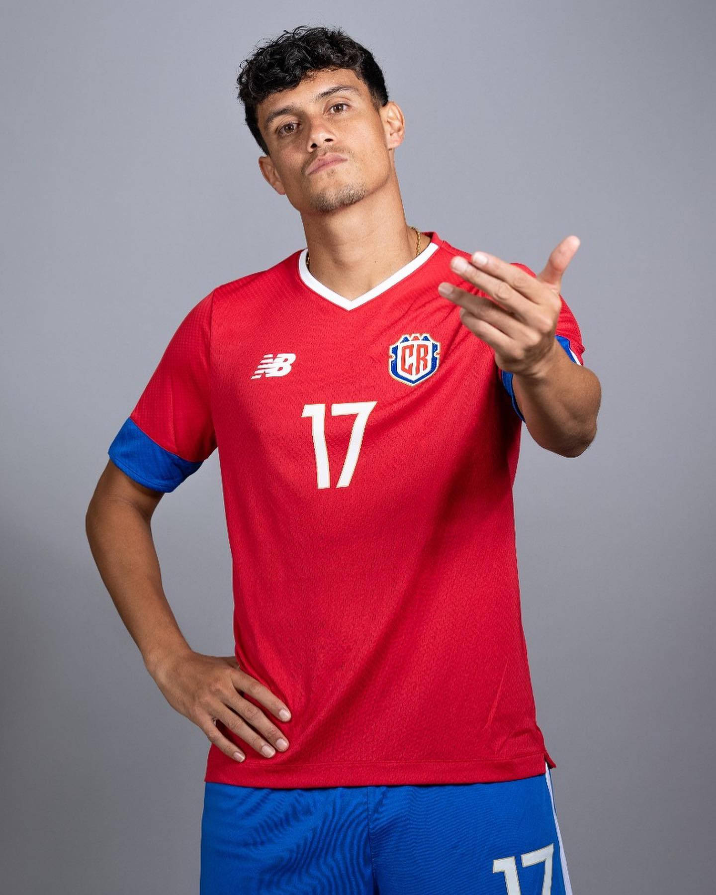 Football Players 桌布 壁紙 — 一位自信的足球運動員身穿紅色球衣，號碼17，在純灰色攝影棚背景前擺姿勢。