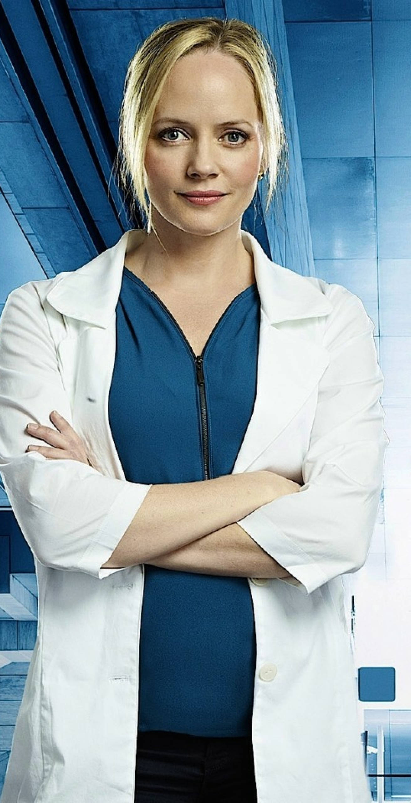 Marley Shelton 桌布 壁紙 — 一位自信的金髮女性穿著白色實驗室外套，雙臂交叉站在藍色臨床背景前。