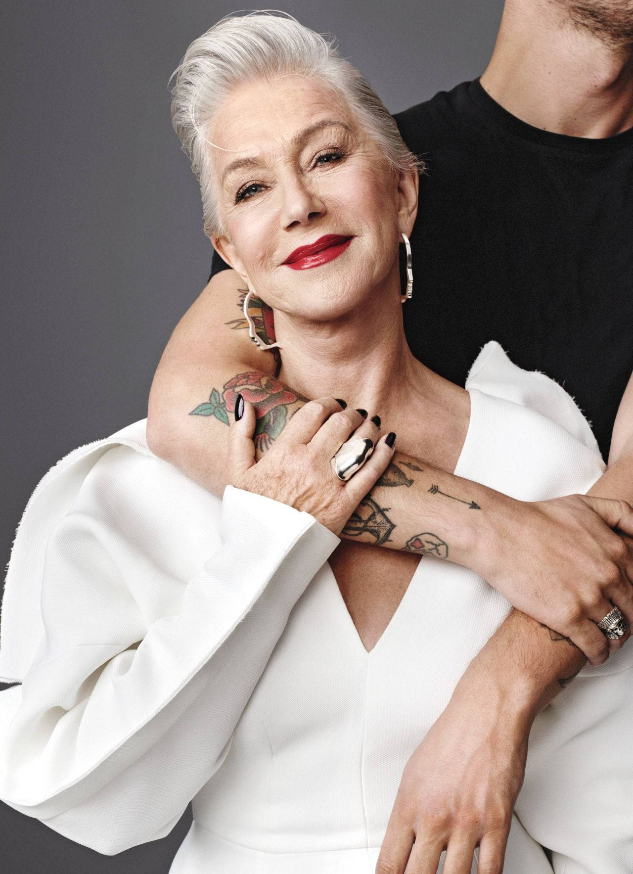 Celebrity 桌布 壁紙 — 一位自信的銀髮紅唇女性微笑著擁抱一位穿黑色襯衫的男性，背景為灰色。