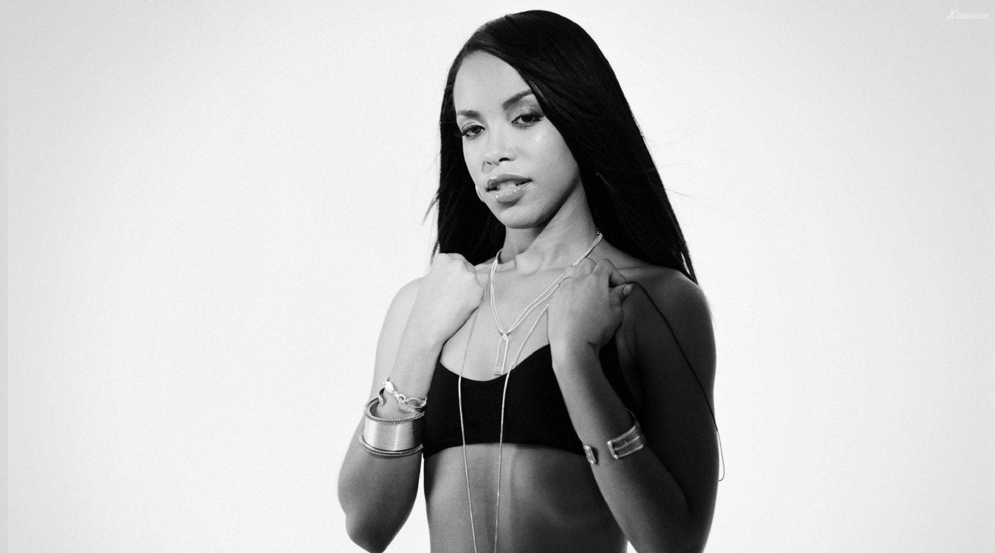 aaliyah 桌布 壁紙 — 一位自信的長黑髮女性，穿著黑色上衣，在單色調的純白背景前擺姿勢。