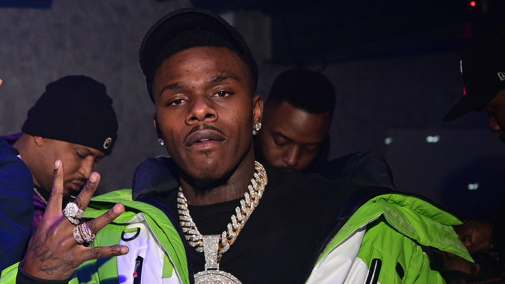 Dababy 桌布 壁紙 — 一位自信的饒舌歌手穿著亮綠色外套和鑽石鏈，在燈光昏暗的派對上比出和平手勢。