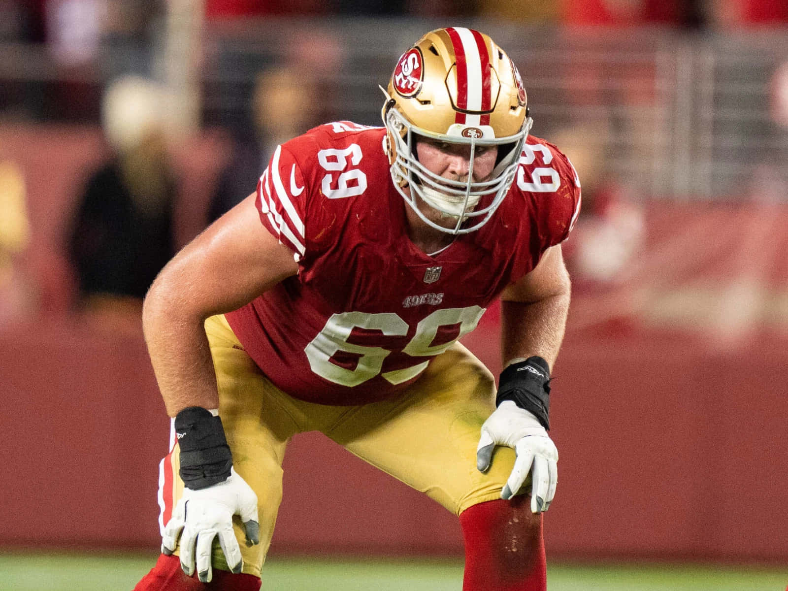 Mike Mcglinchey 桌布 壁紙 — 一位舊金山49人美式足球員身穿紅金色球衣，在球場燈光下激烈地蹲伏。