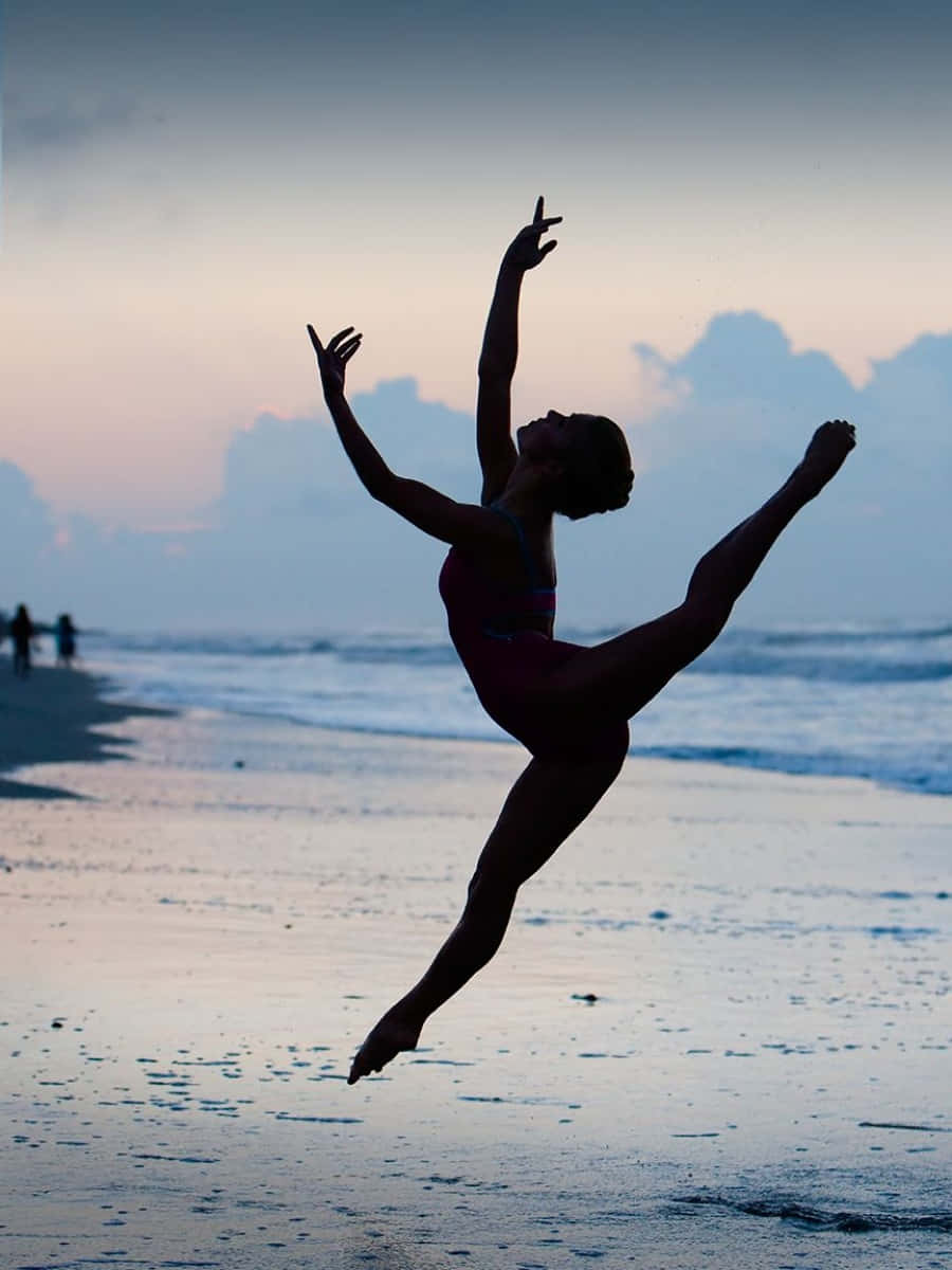 dancer 桌布 壁紙 — 一位舞者在黃昏的海灘上以剪影跳躍，雙臂高舉，一條腿高高伸展，映襯著柔和的粉彩天空。