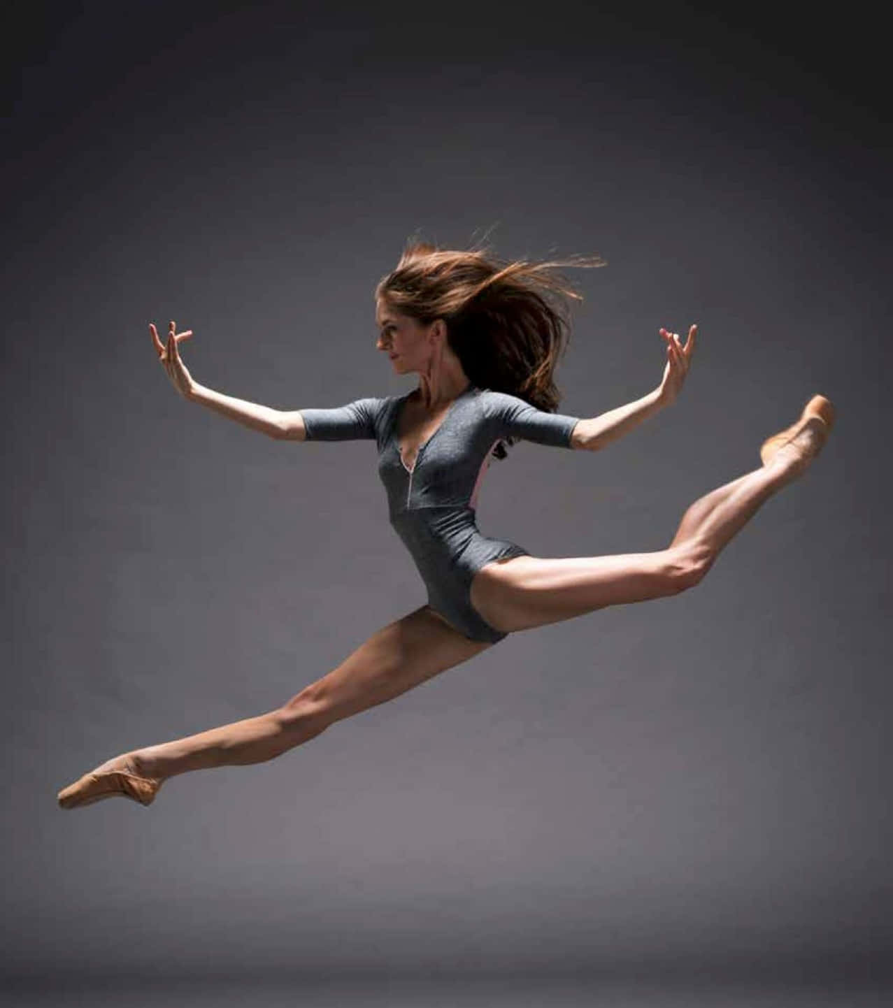 dancer 桌布 壁紙 — 一位芭蕾舞者在深灰色工作室背景前，以動態劈腿姿勢躍起空中。