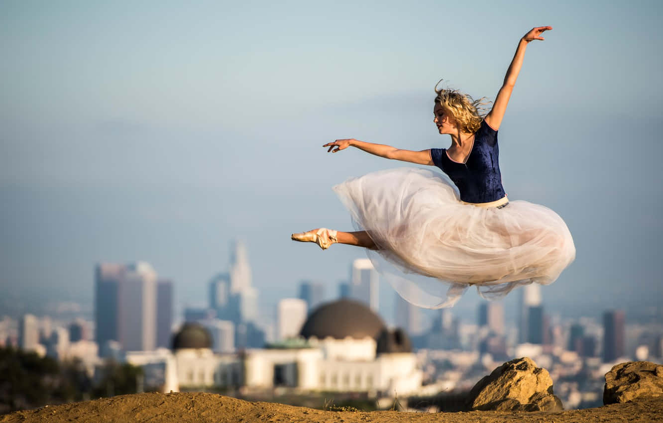 Ballet 桌布 壁紙 — 一位芭蕾舞者在空中優雅地躍起，背景是模糊的城市天際線和一個圓頂天文台。