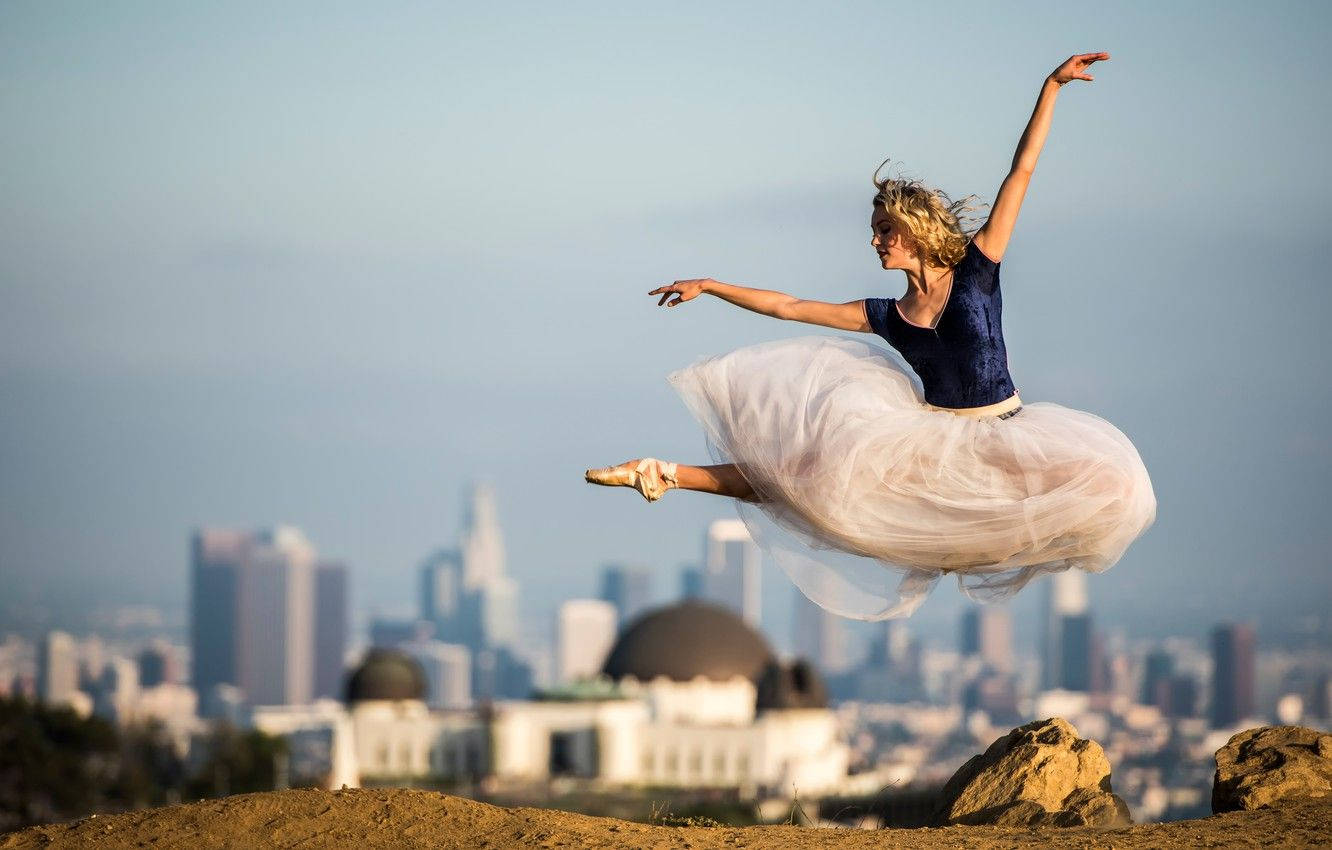 Ballet 桌布 壁紙 — 一位芭蕾舞者在空中優雅地躍起，背景是朦朧的城市天際線，前景是圓頂天文台。