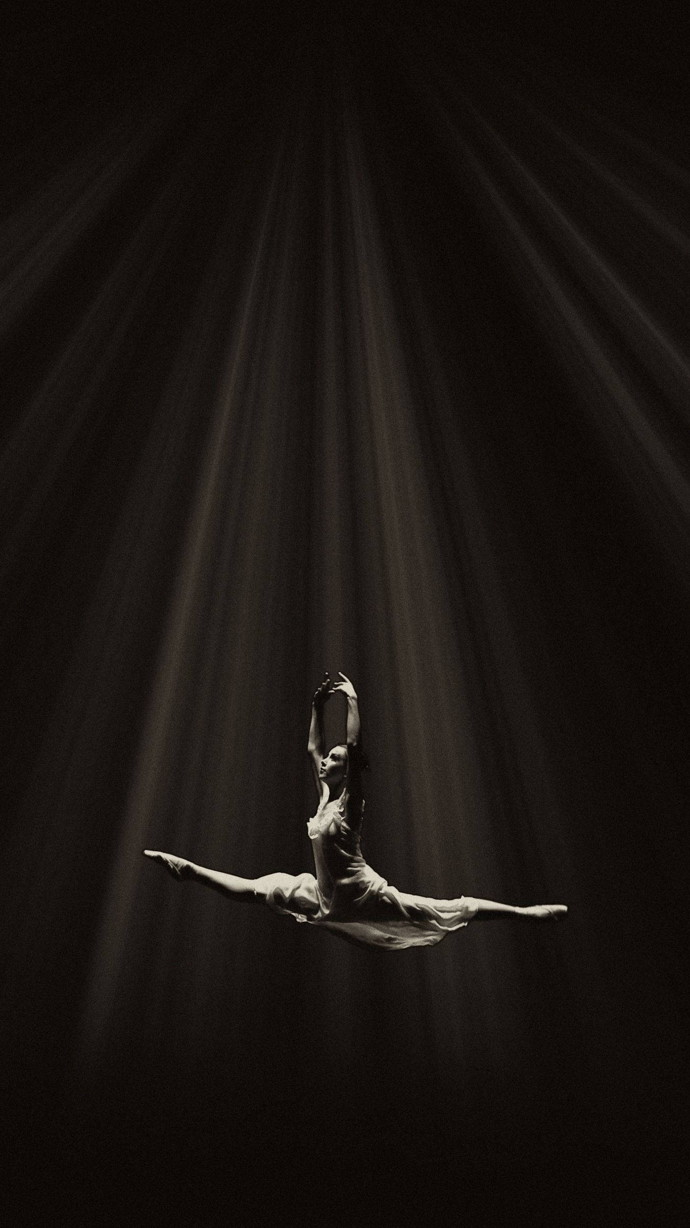 ballerina 桌布 壁紙 — 一位芭蕾舞者在黑暗虛空中，於戲劇性的聚光燈光束下優雅地凌空劈腿。