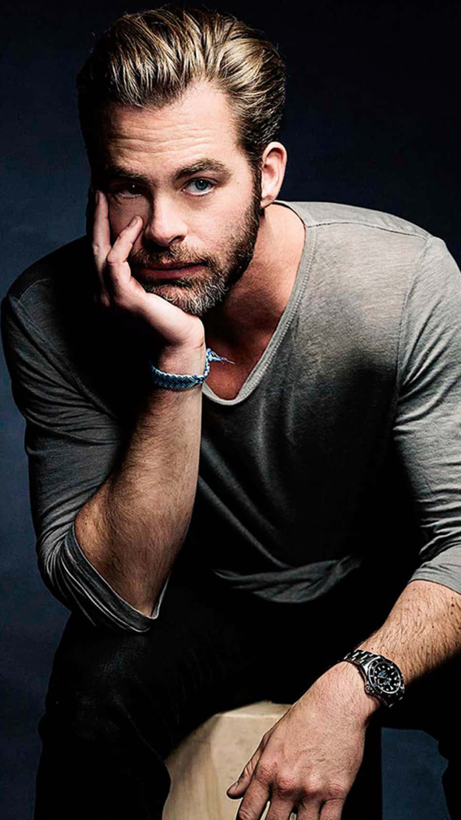 actor 桌布 壁紙 — 一位英俊的男子，頭髮和鬍子經過造型，在深色背景下用手托著下巴，穿著灰色襯衫和手錶。