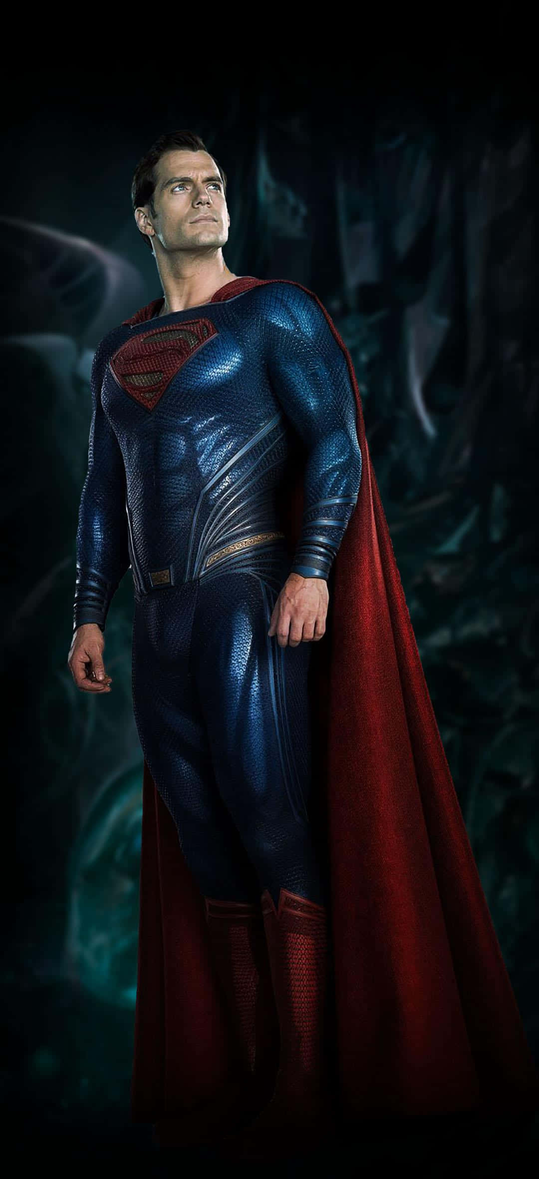 Zack Snyders Justice League 桌布 壁紙 — 一位英勇的超級英雄，身穿質感藍色套裝，披著飄逸的紅色斗篷，在黑暗岩石背景下高高站立。