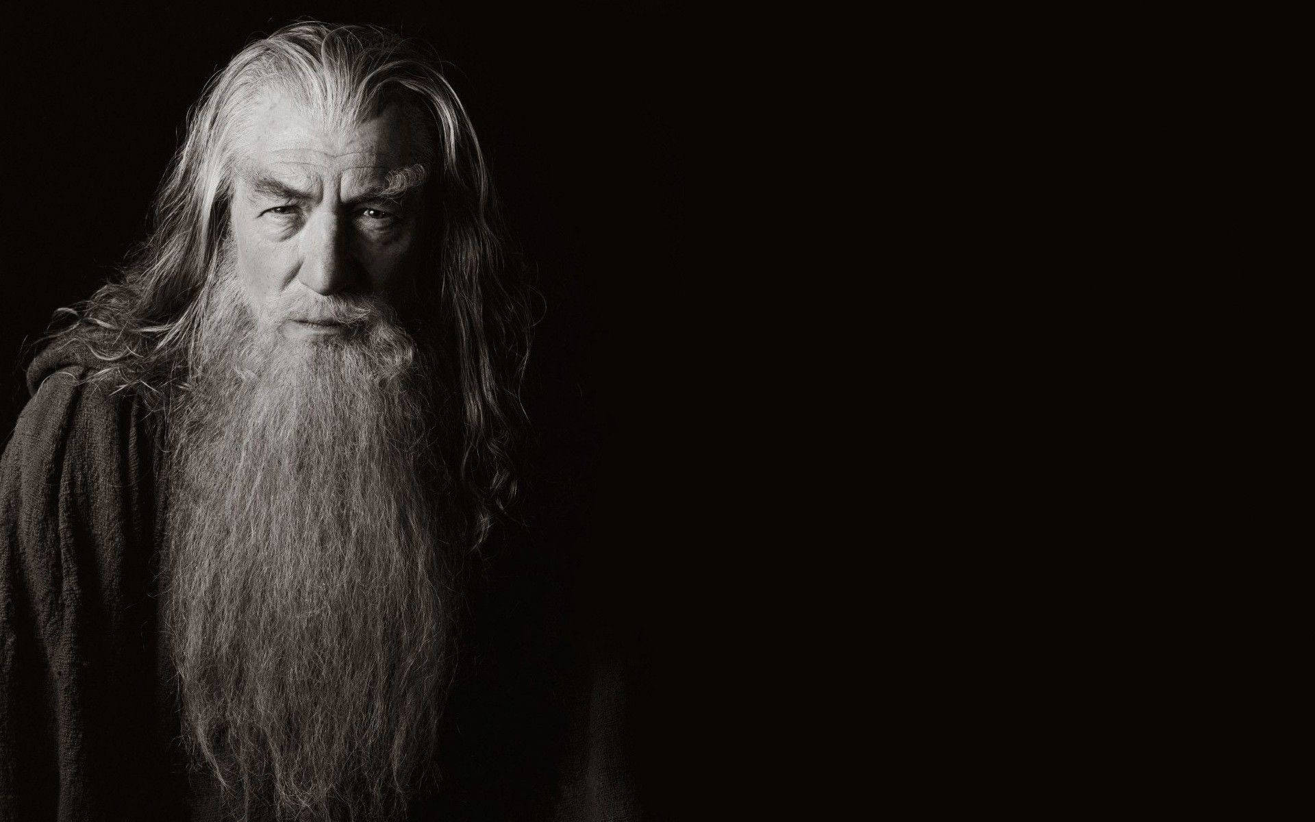 Gandalf 桌布 壁紙 — 一位莊嚴的巫師，長長的白髮和鬍鬚，在單色的漆黑背景下凝視著。