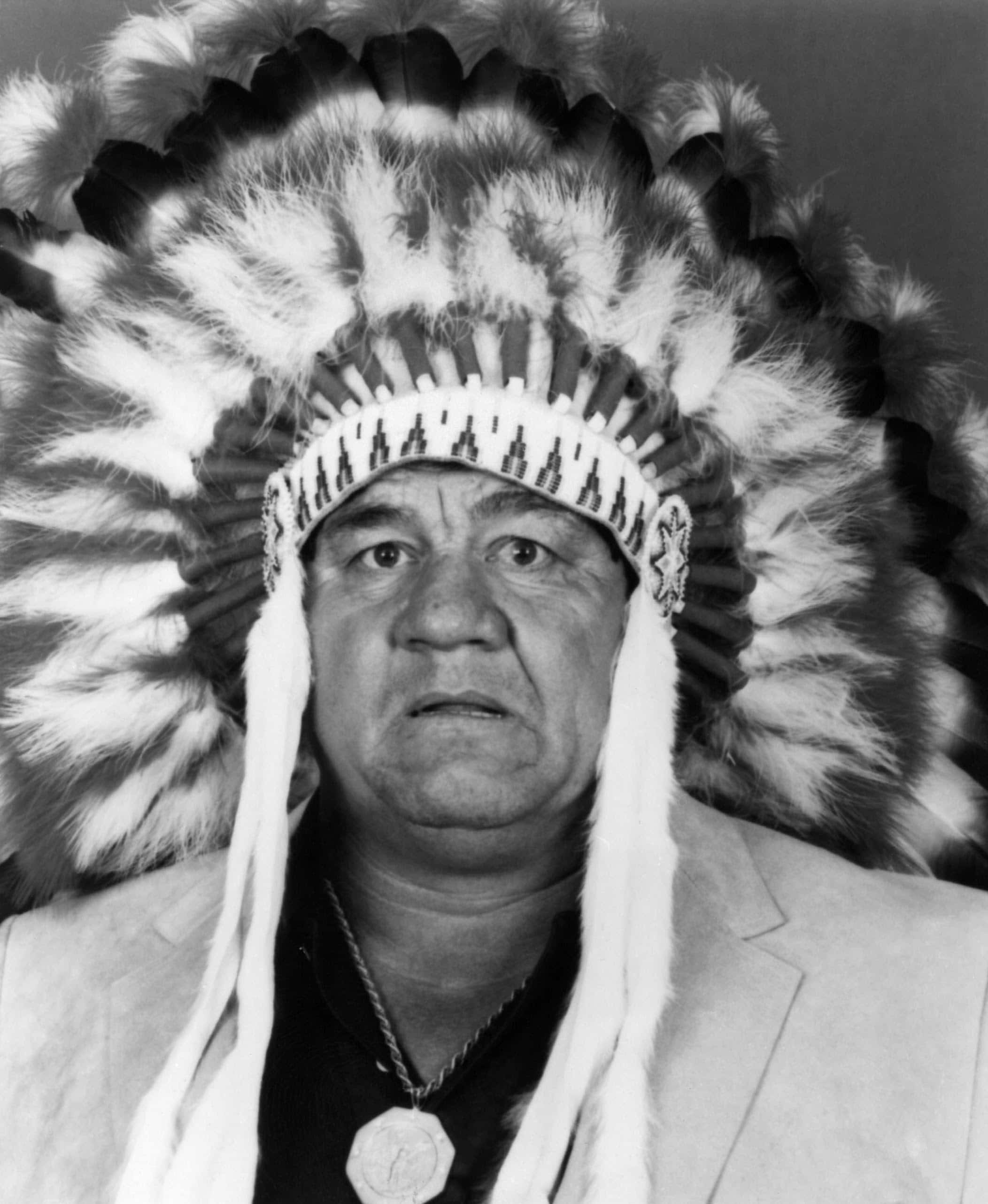 Native American 桌布 壁紙 — 一位莊嚴的男子戴著傳統羽毛頭飾，在黑白肖像中直視鏡頭。