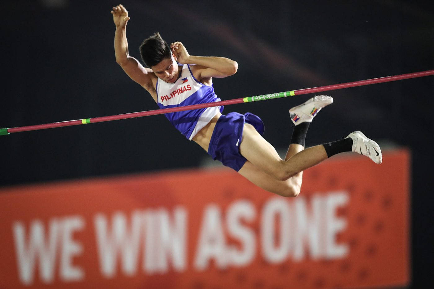 Athletic 桌布 壁紙 — 一位菲律賓男跳高選手在體育場燈光下以戲劇性的空中姿勢越過橫桿。