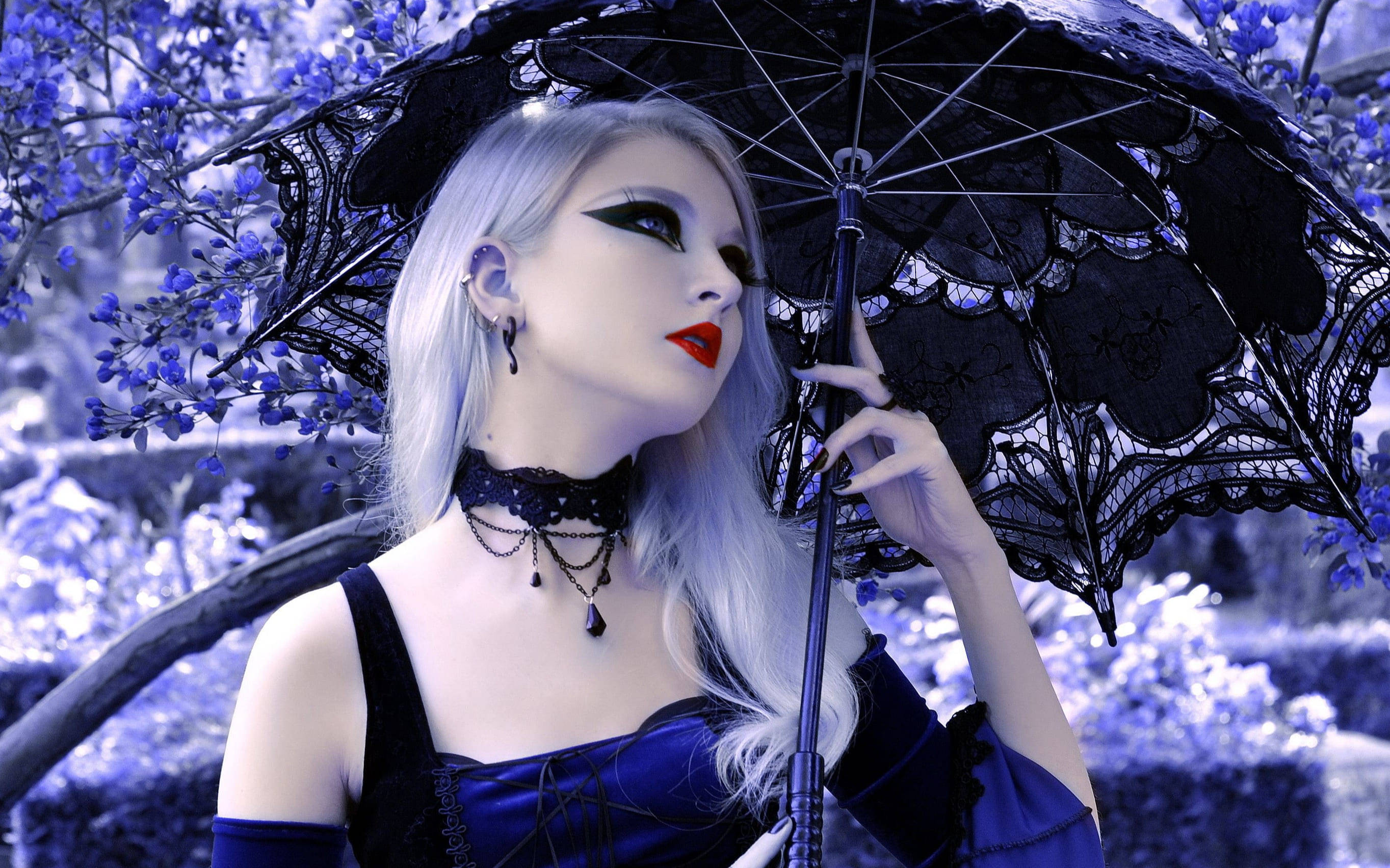 Goth 桌布 壁紙 — 一位蒼白的銀髮女子，化著大膽的妝容，在藍色調的花園中撐著一把黑色蕾絲陽傘。