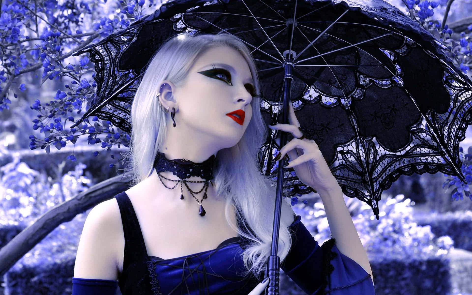 Goth 桌布 壁紙 — 一位蒼白的銀髮女子化著大膽妝容，在藍色調的花園中手持一把黑色蕾絲陽傘。