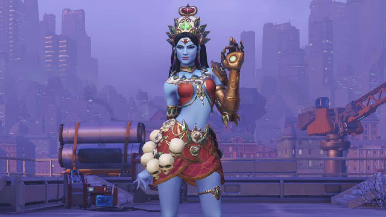 Overwatch Symmetra 桌布 壁紙 — 一位藍皮膚的女神，戴著金色王冠和華麗盔甲，自信地站在屋頂上，背景是朦朧的紫色城市景觀。